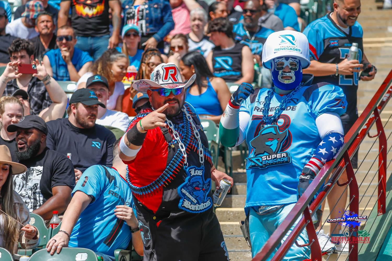 Two people dressed in colorful costumes and face paint, surrounded by a crowd of spectators at an outdoor event.