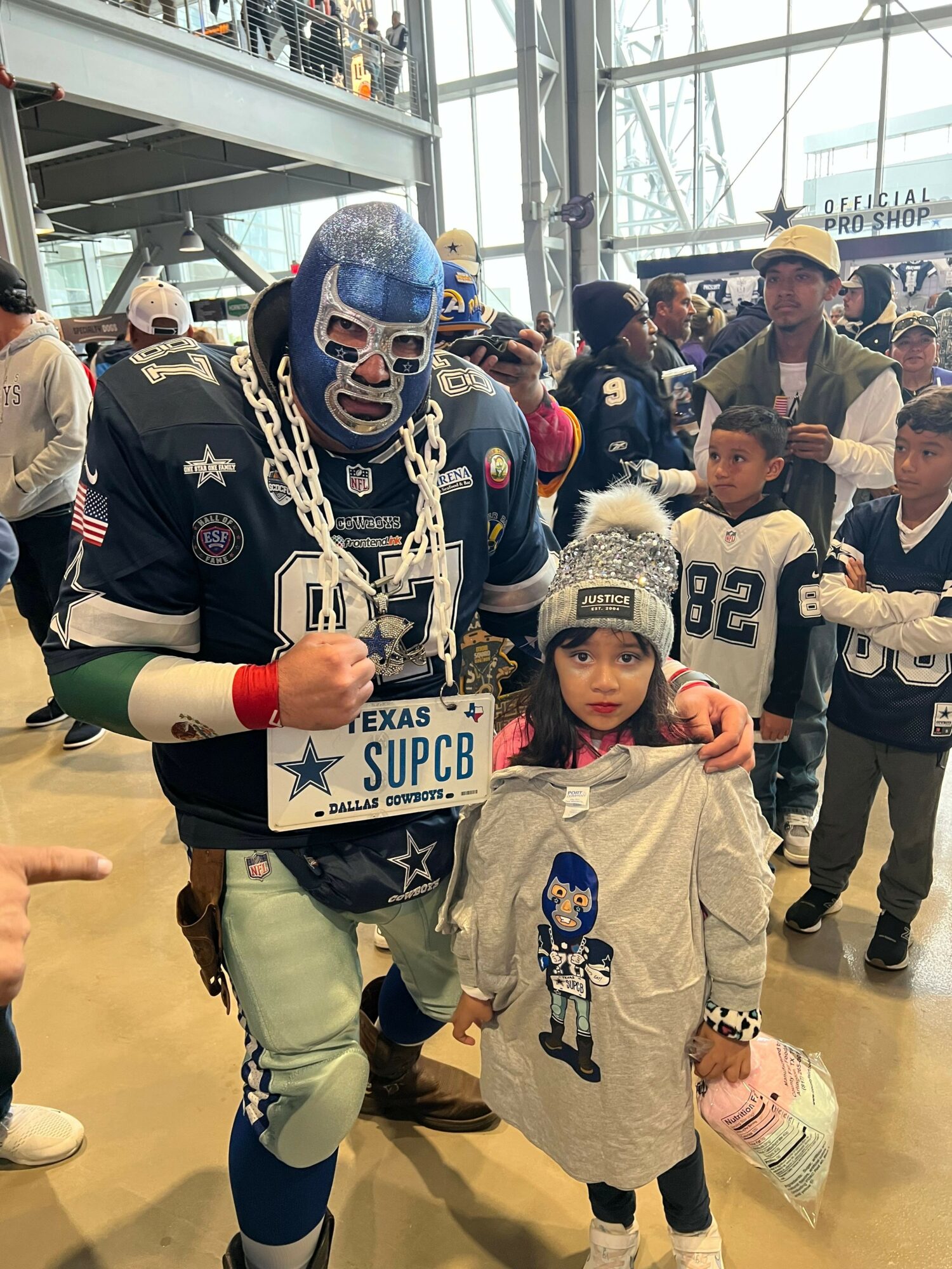 Group of children and adults at an indoor sports event, some in football jerseys, with a child holding a Dallas Cowboys sign.