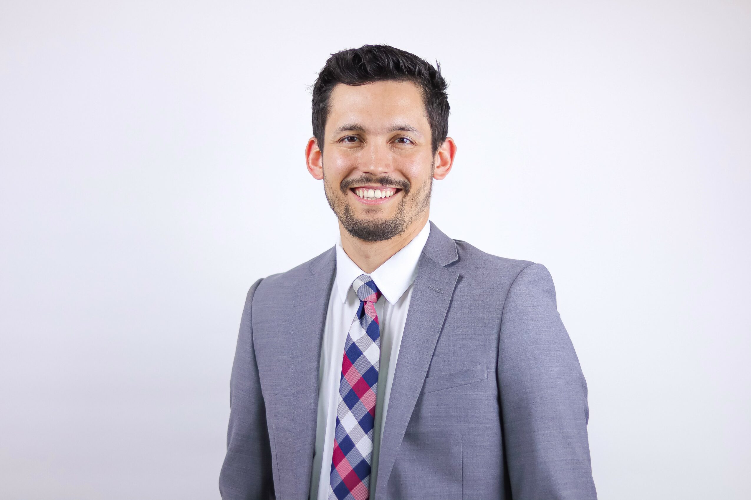 Man in a gray suit with a colorful tie, smiling, against a plain white background.