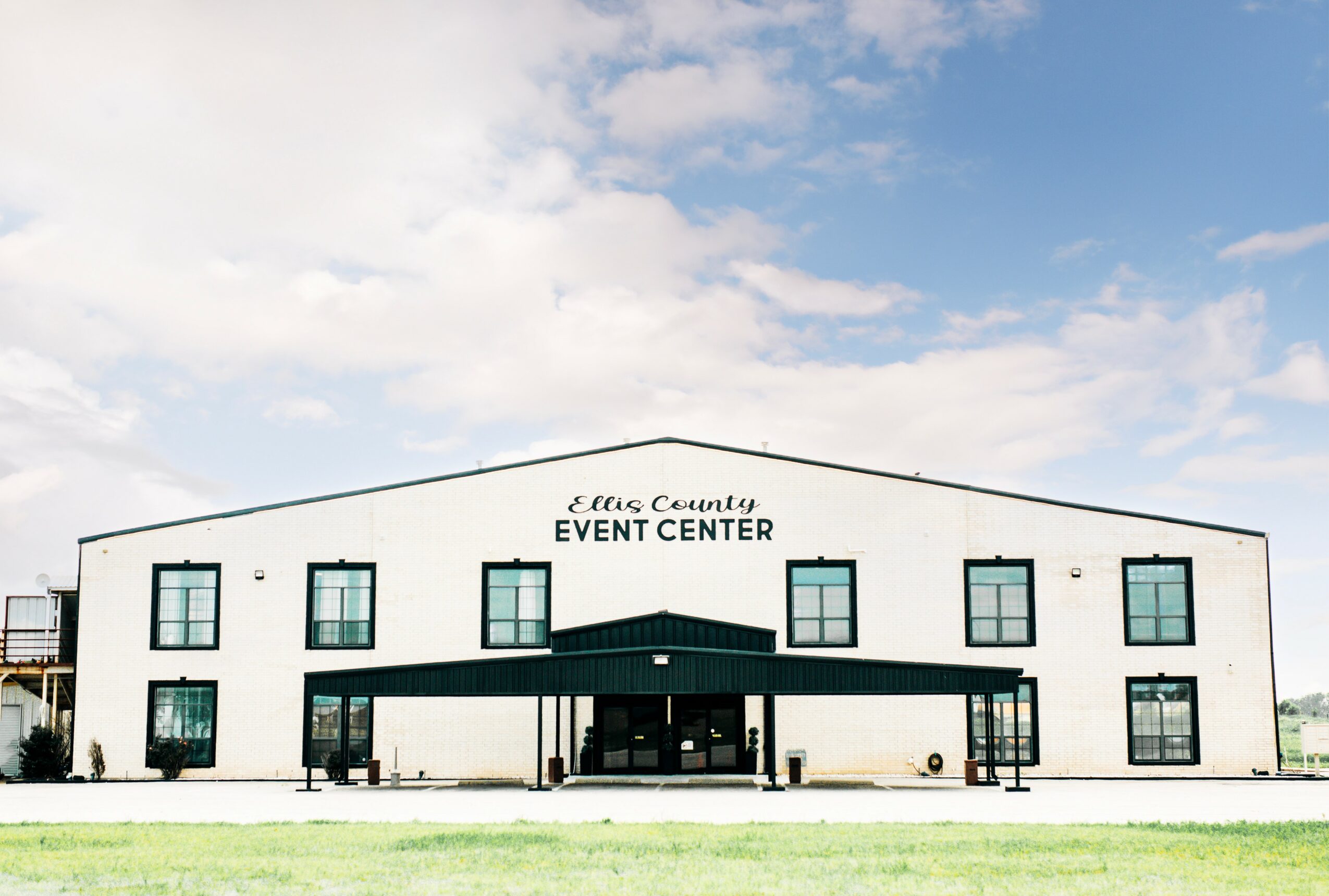 Two-story white event center building with black trim and multiple windows, under a partly cloudy sky.