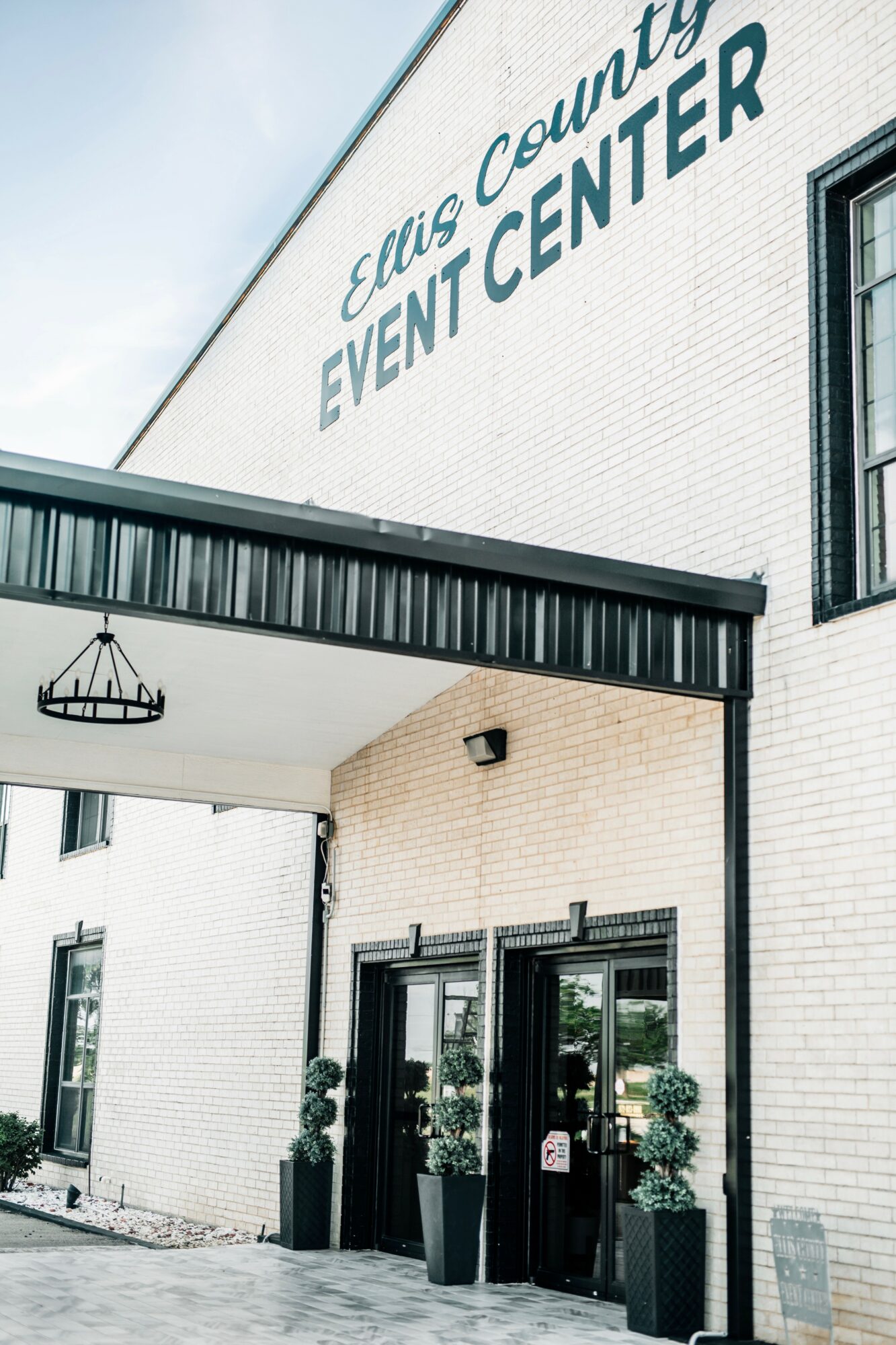 Exterior view of Elmore County Event Center with entrance doors and potted plants, clear sky in background.
