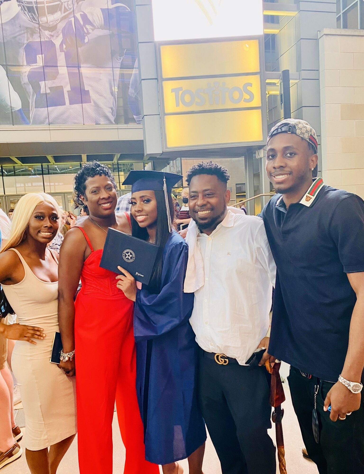 Group of five people, one in graduation gown and cap, smiling outdoors near a Taco Bell sign.