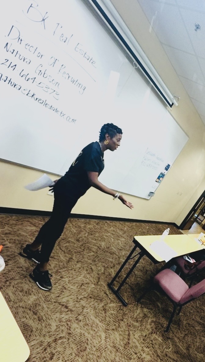 Person standing and pointing at a whiteboard with handwritten notes, in a classroom setting.