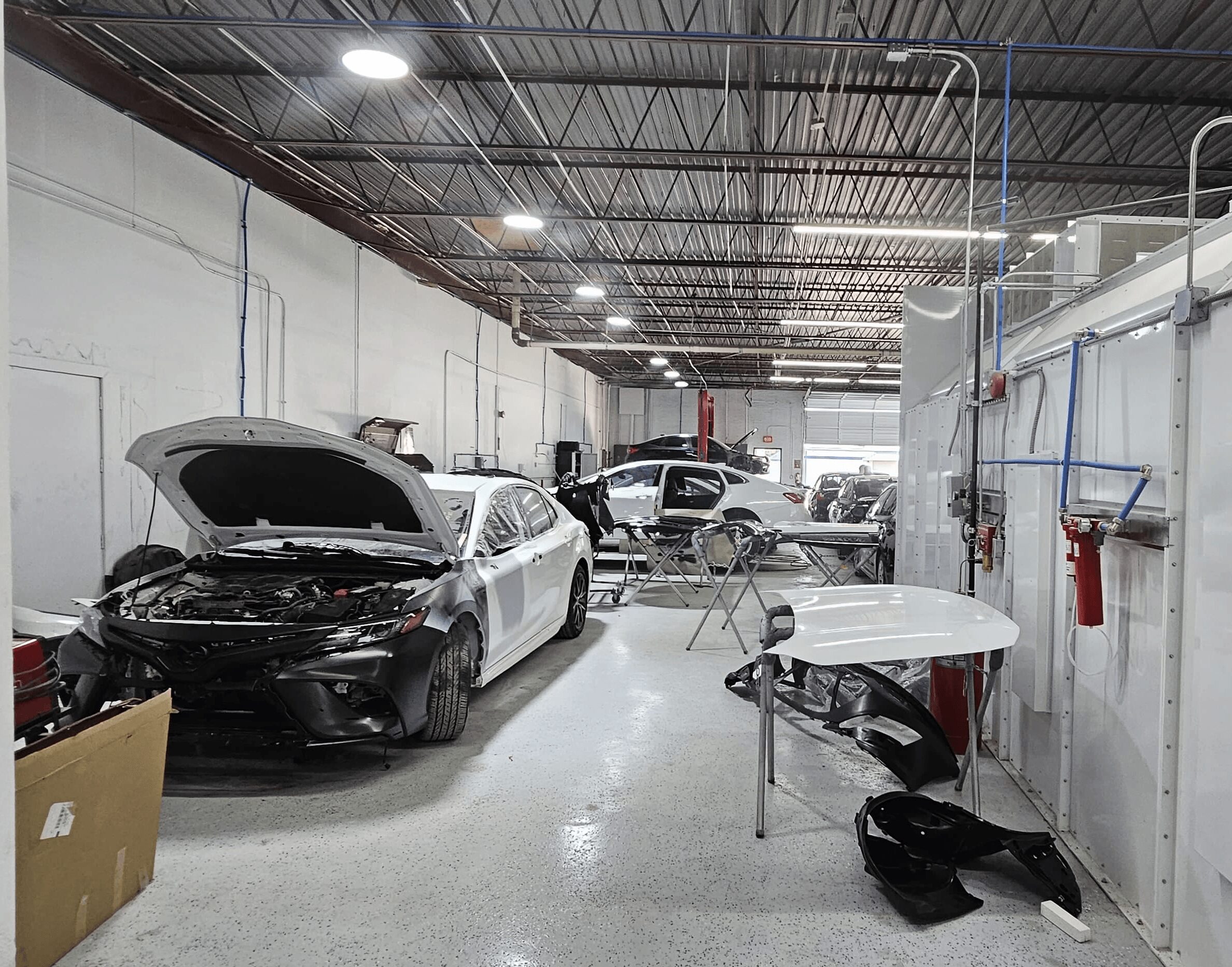 Indoor garage with multiple cars, some with open hoods, and work tables with tools and equipment.