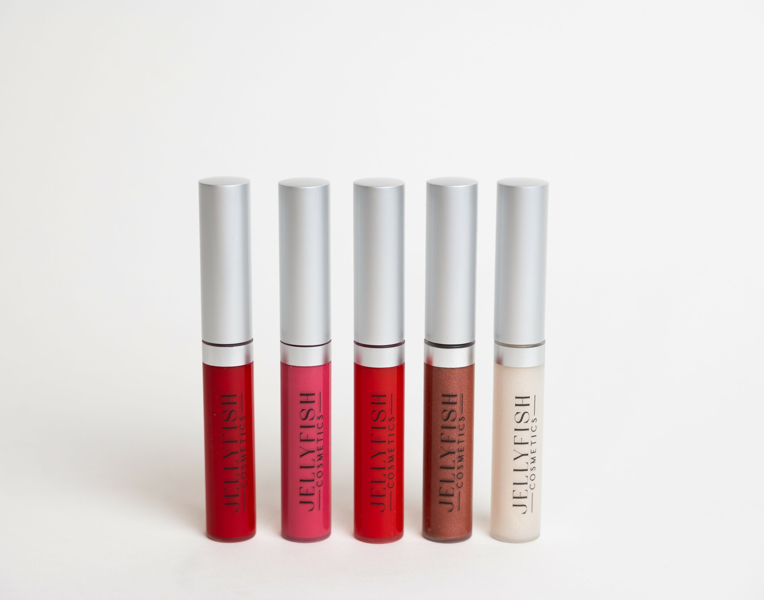 Five lip gloss tubes with silver caps and pink, red, brown, and beige labels, standing upright on a white background.