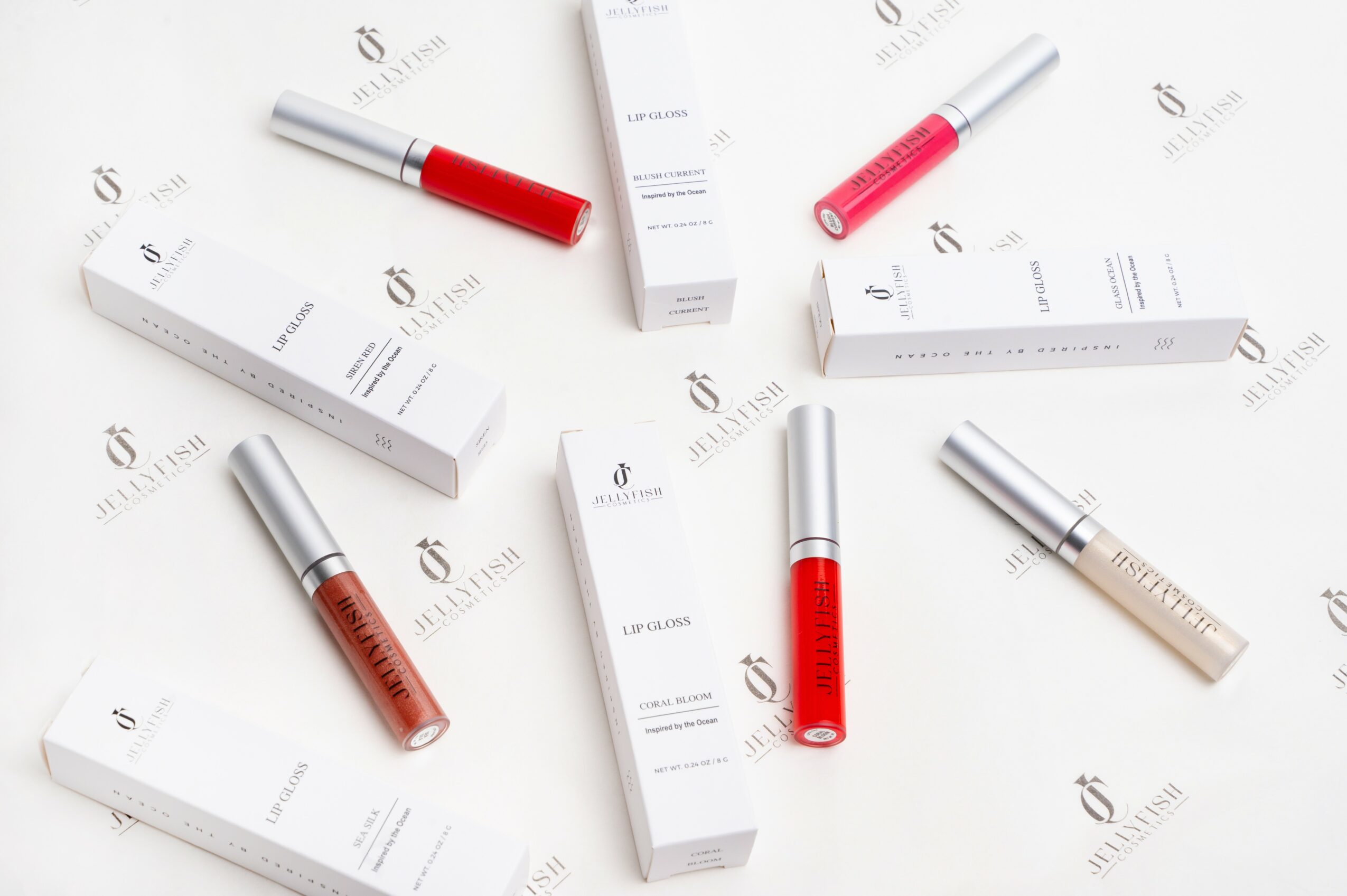 Lip gloss tubes and boxes arranged on a white surface, with some tubes lying down and others standing upright.