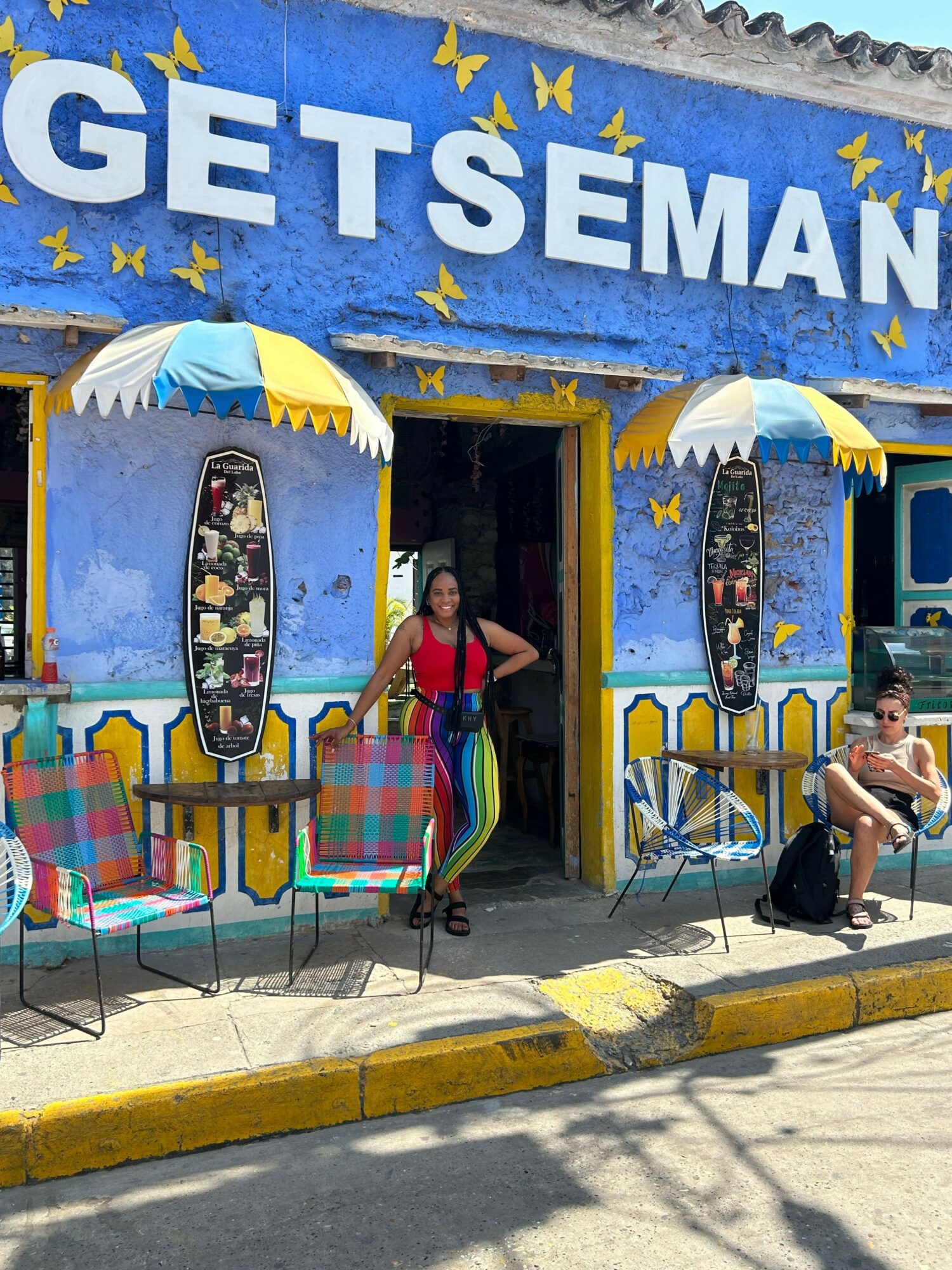 People standing outside a blue building with a sign that reads 'GET SEMAN' and colorful chairs, umbrellas, and a yellow curb.