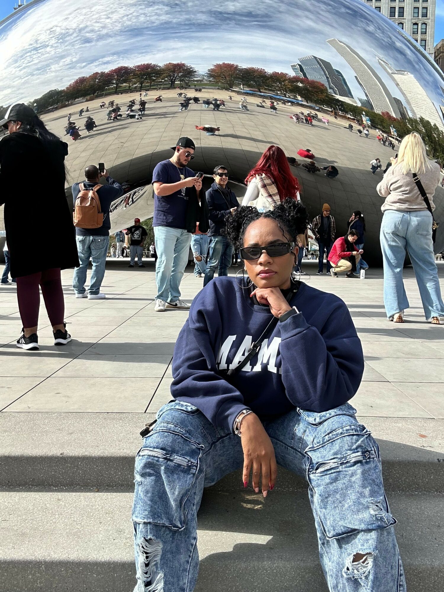 Person taking a selfie outdoors with a group of people and a large white structure in the background.