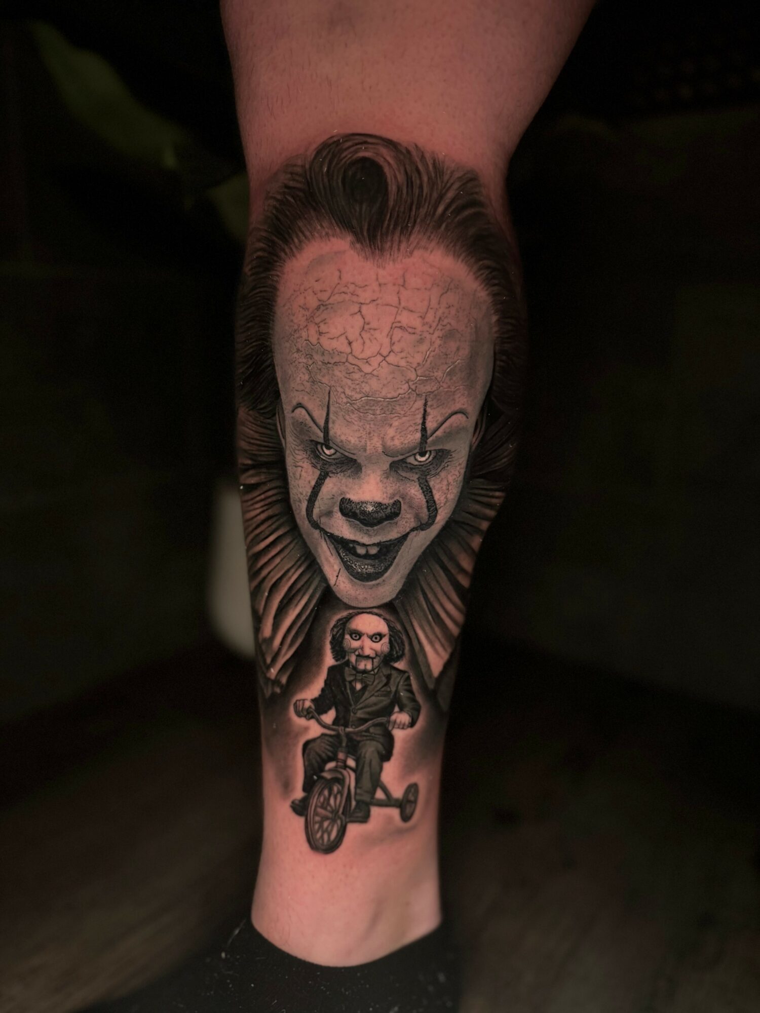 Tattoo of a clown face with makeup and a person riding a motorcycle below it on a person's leg.