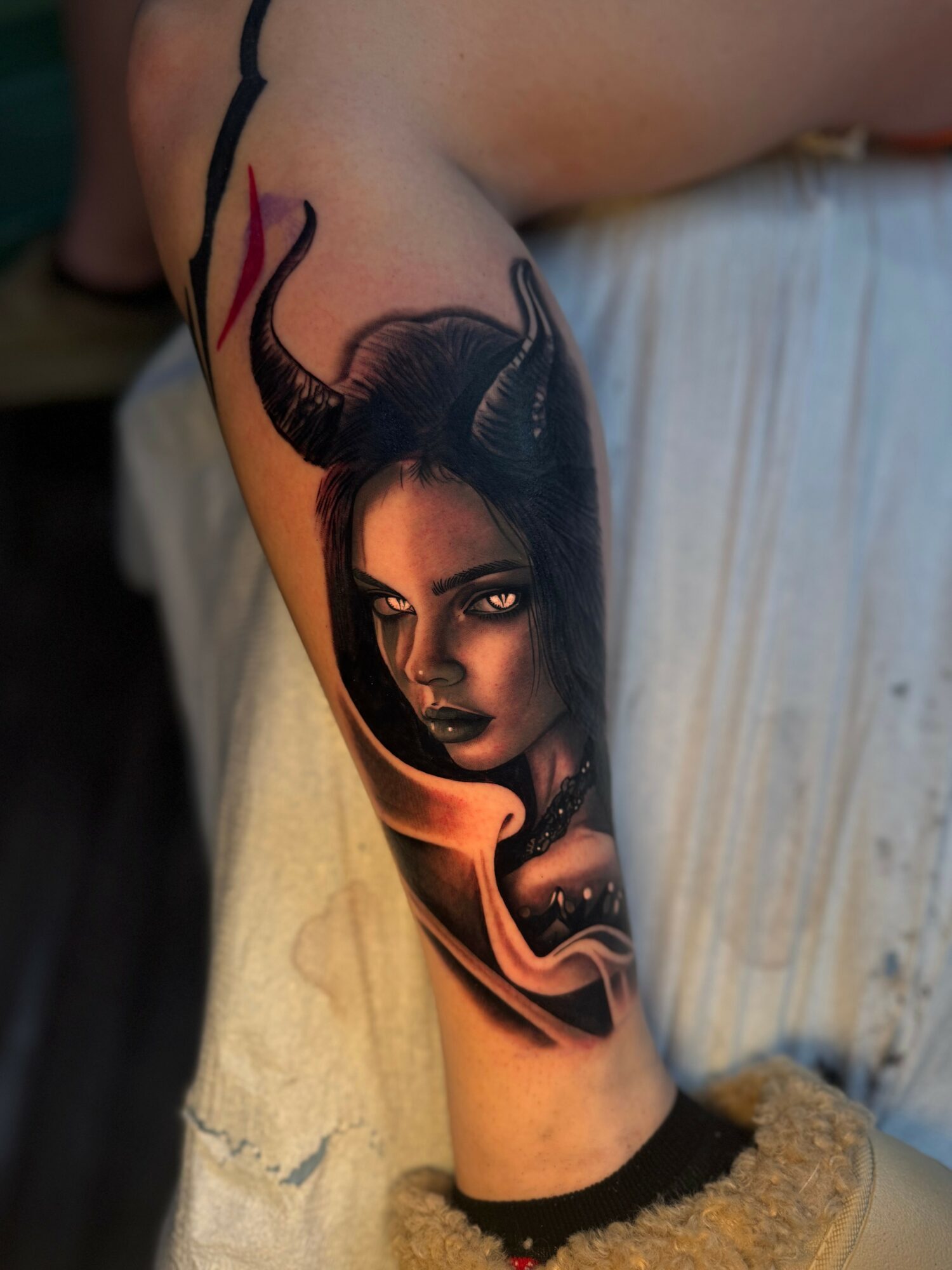 Tattoo of a woman with dark hair and horns, surrounded by flames, on a person's arm.