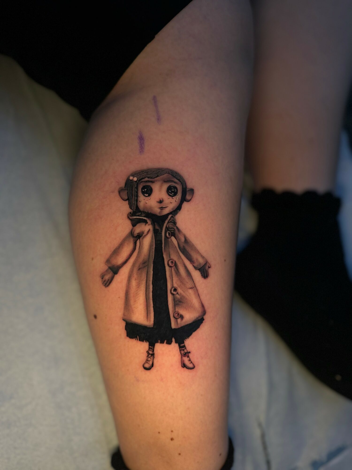 Tattoo of a bear wearing a coat on person's leg, with purple markings above. Person wears black socks.