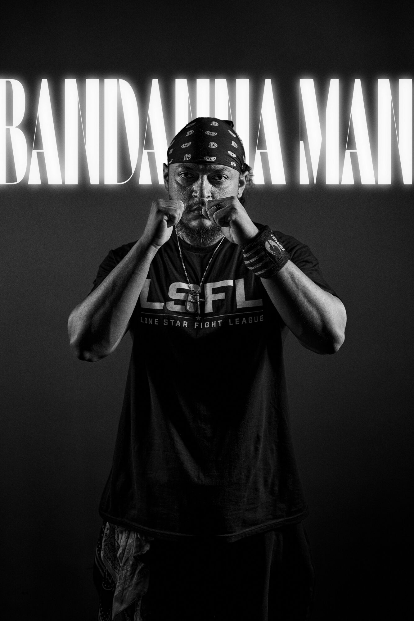 Person wearing a bandana and glasses, standing in front of a sign that reads 'BAINDANA MAI', with hands near face.