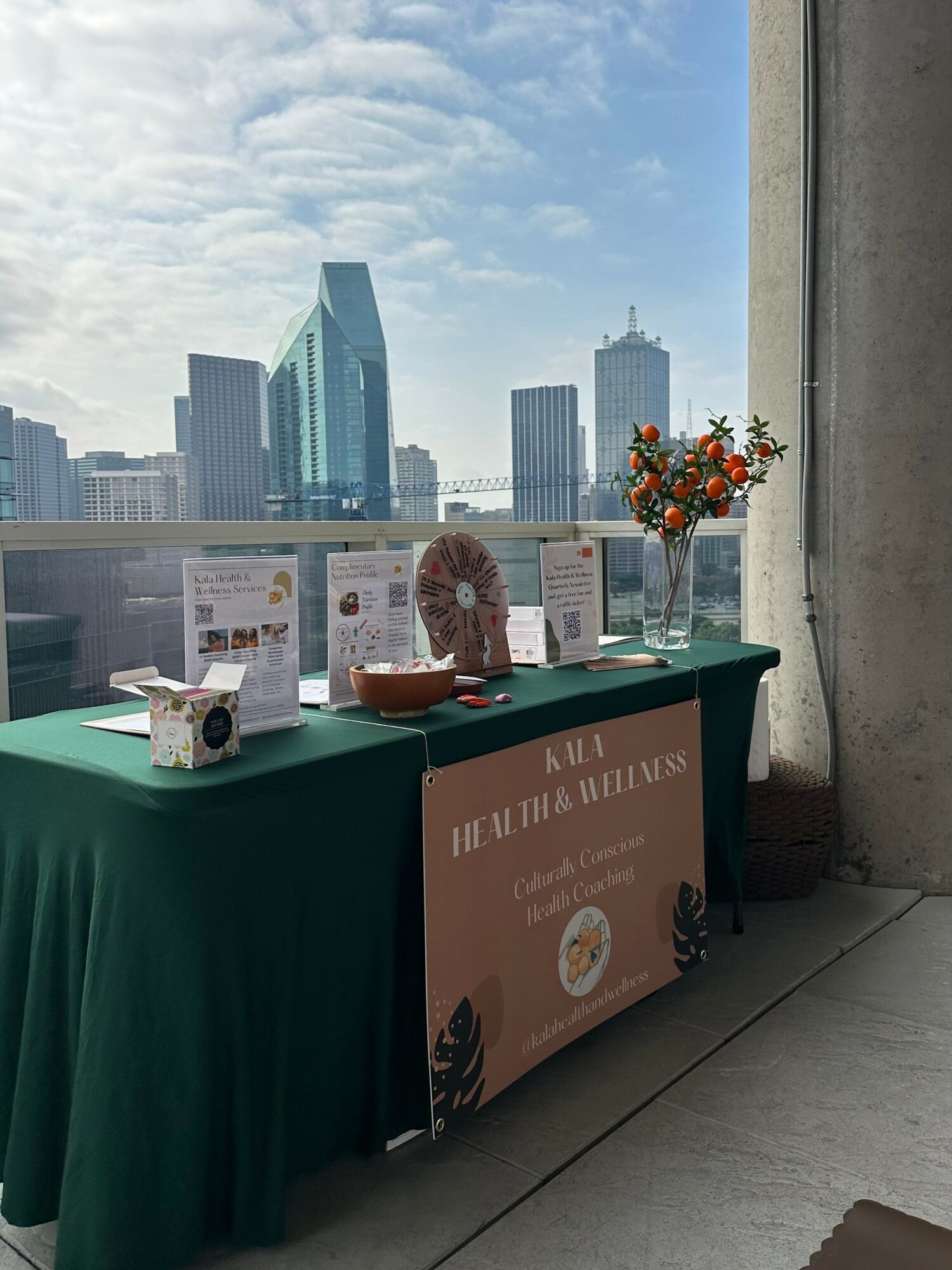 Table with promotional materials and a flower arrangement against a city skyline with tall buildings and a partly cloudy sky.