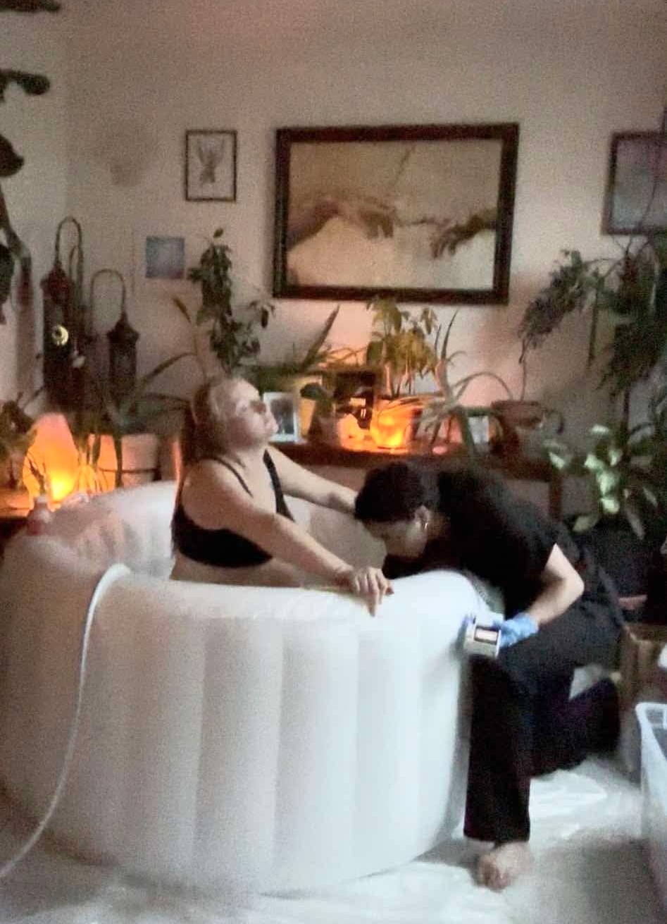Two people sit on a white sofa in a cozy, decorated living room with plants and warm lighting.
