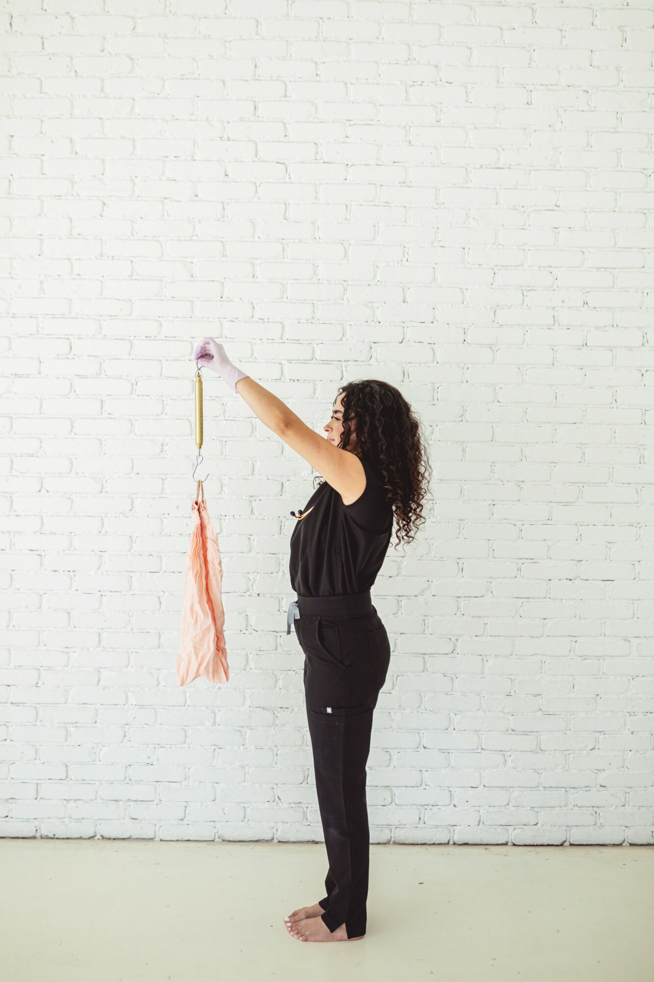 Person with curly hair holding a tassel in front of a white brick wall, standing sideways.