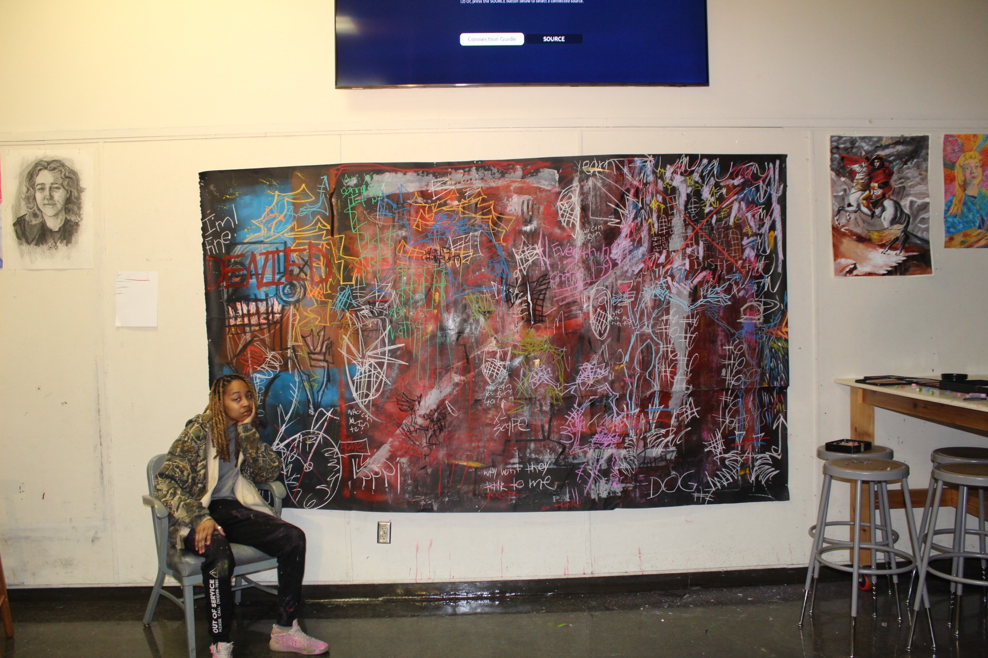 Person sitting on a stool in front of a large, colorful abstract painting in an art gallery.