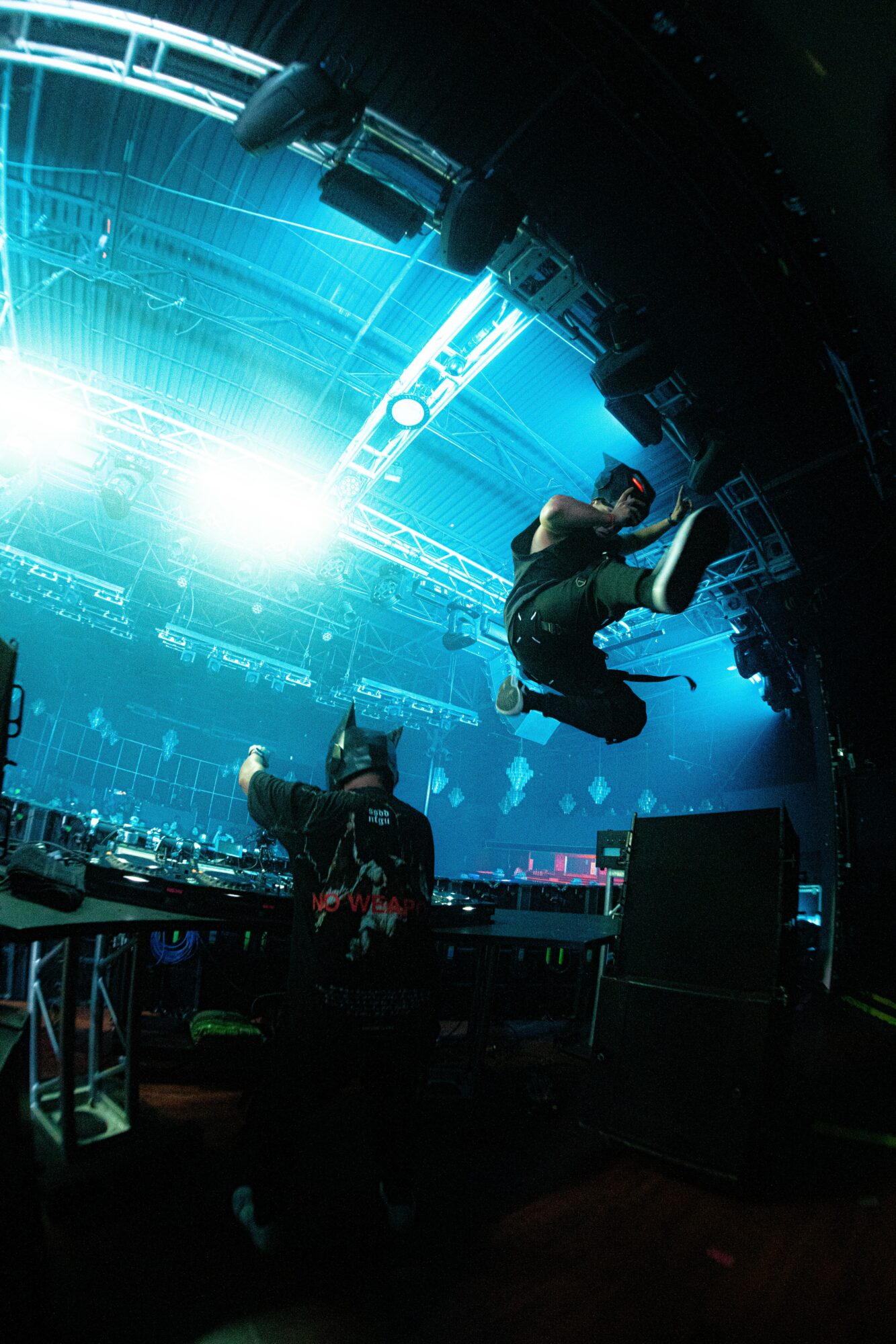 Two people are performing acrobatic stunts on a stage with bright blue lights and a large screen in the background.