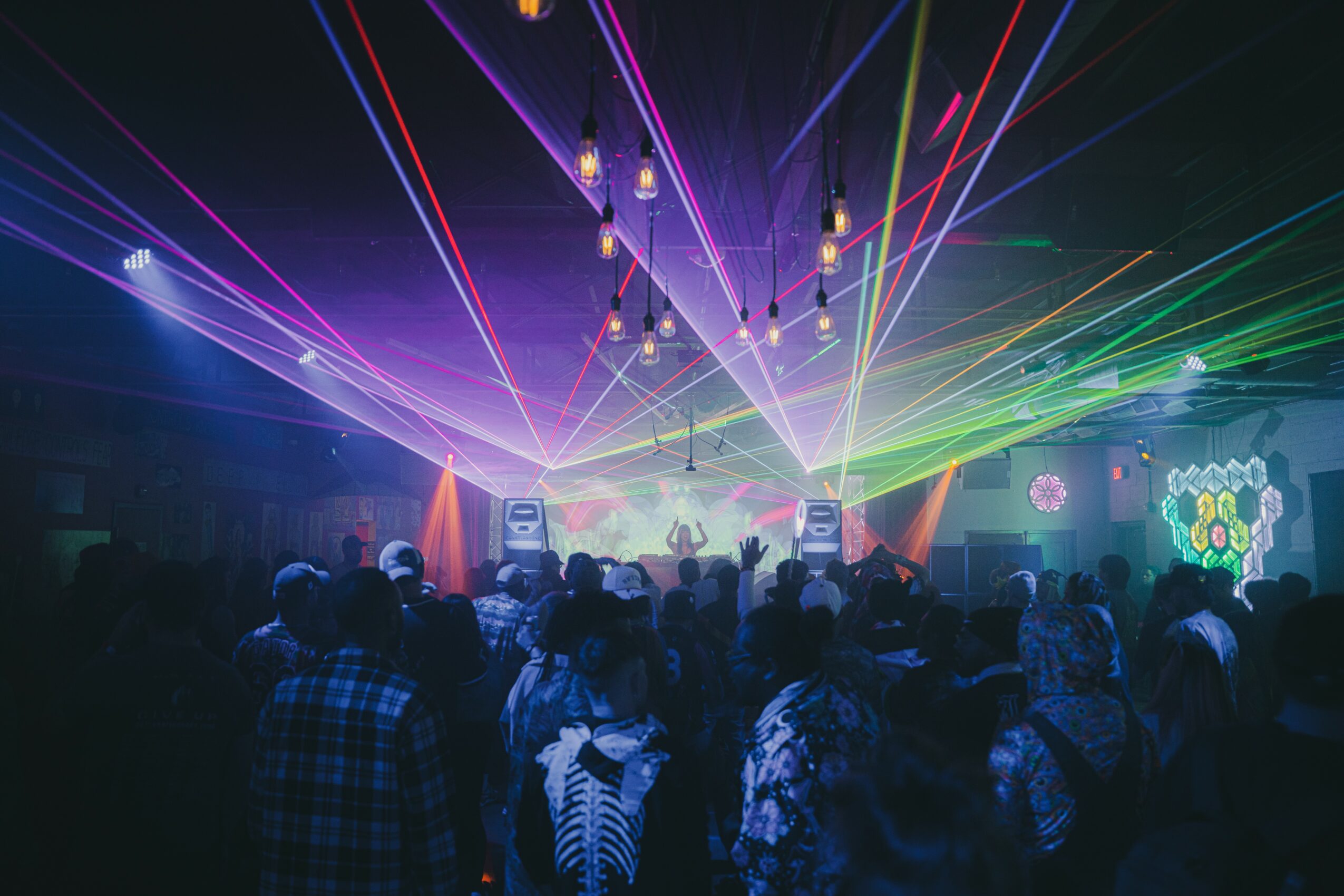 Crowd at a concert with colorful laser lights and stage effects, people dancing and enjoying the event.