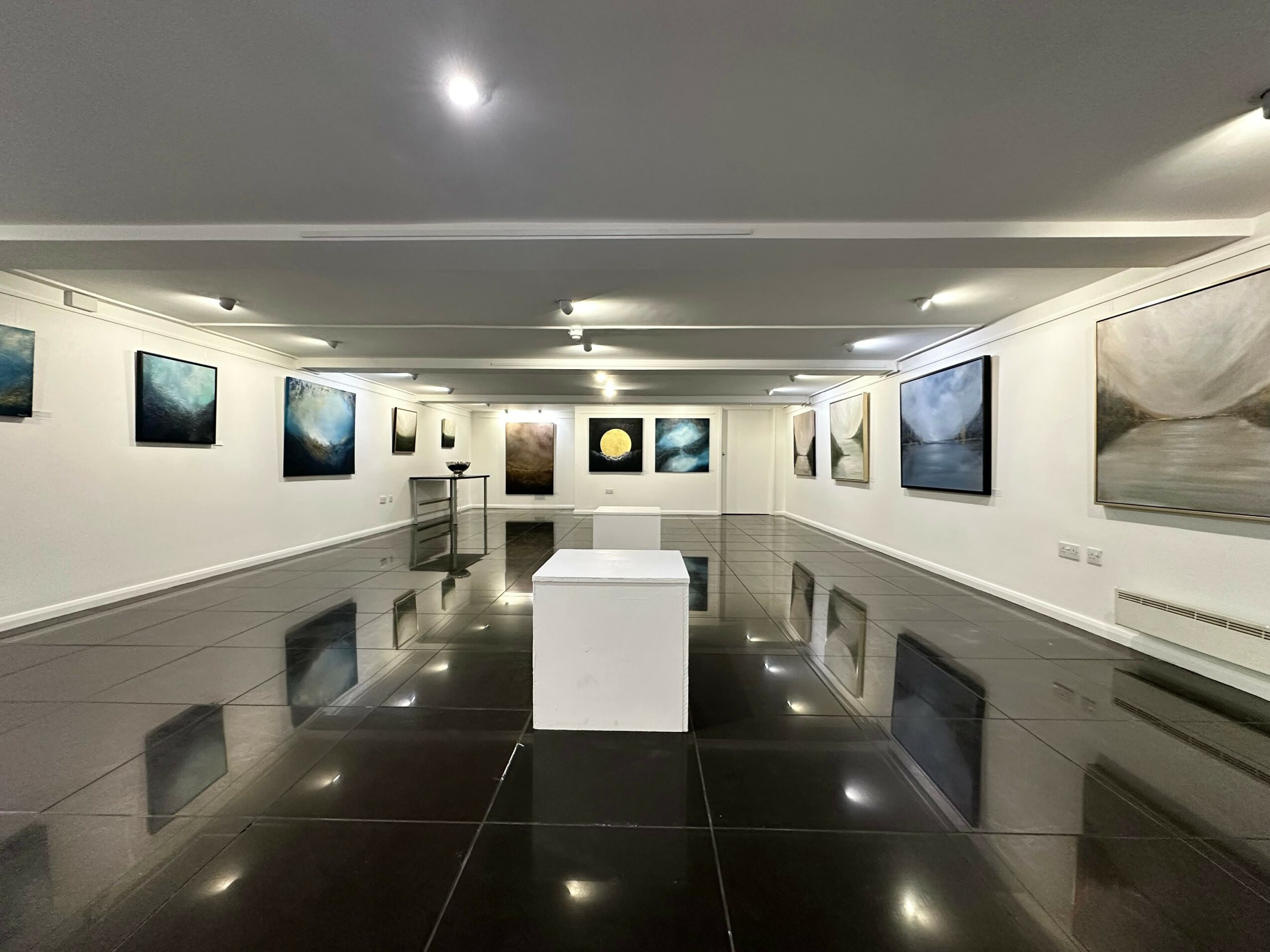 Art gallery with paintings on white walls, a white pedestal in the center, and a reflective black floor.