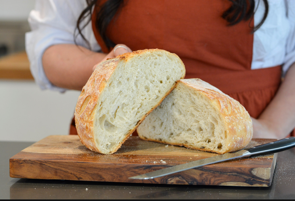 Person in apron holding a sliced loaf of bread on a wooden cutting board with a knife nearby