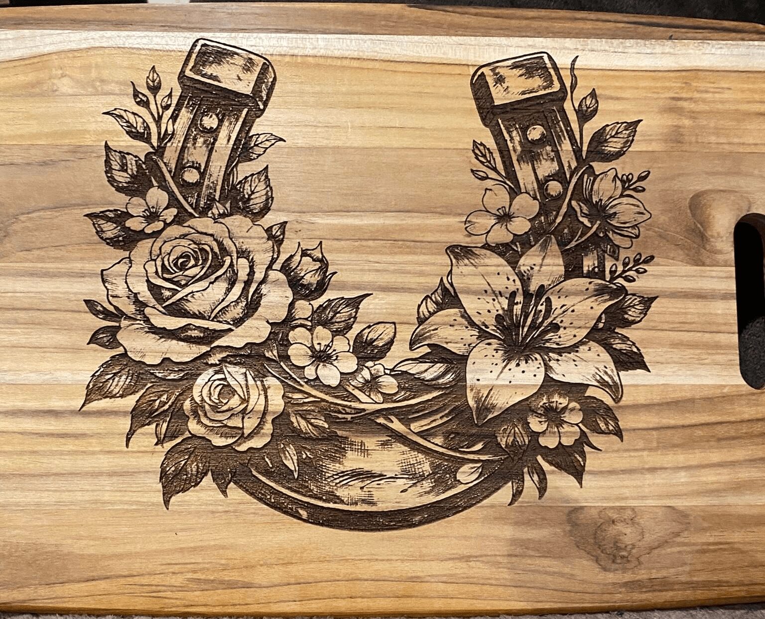 Wooden surface with a floral tattoo design featuring roses, lilies, and two candles, arranged in a U-shape.