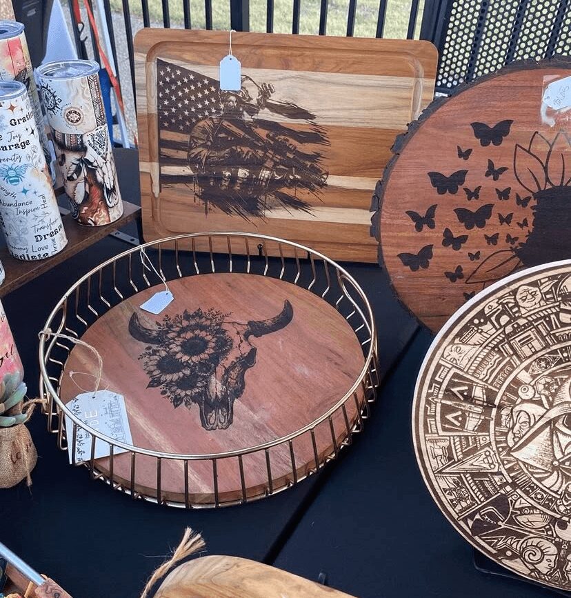 Decorative wooden trays with animal and nature designs, displayed on a table, including a buffalo skull, butterflies, and geometric patterns.