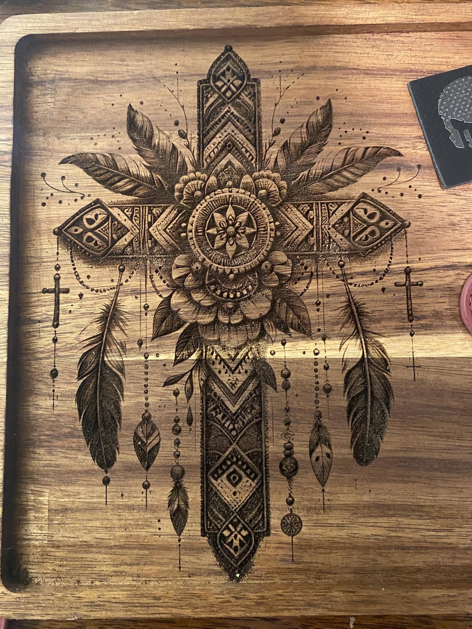Decorative cross with feathers, flowers, and geometric patterns on wooden surface.