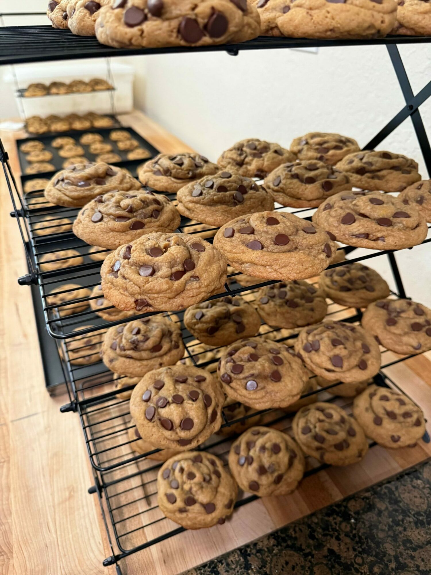 Multiple chocolate chip cookies on a wire rack, with some cookies overlapping each other, on a wooden surface.