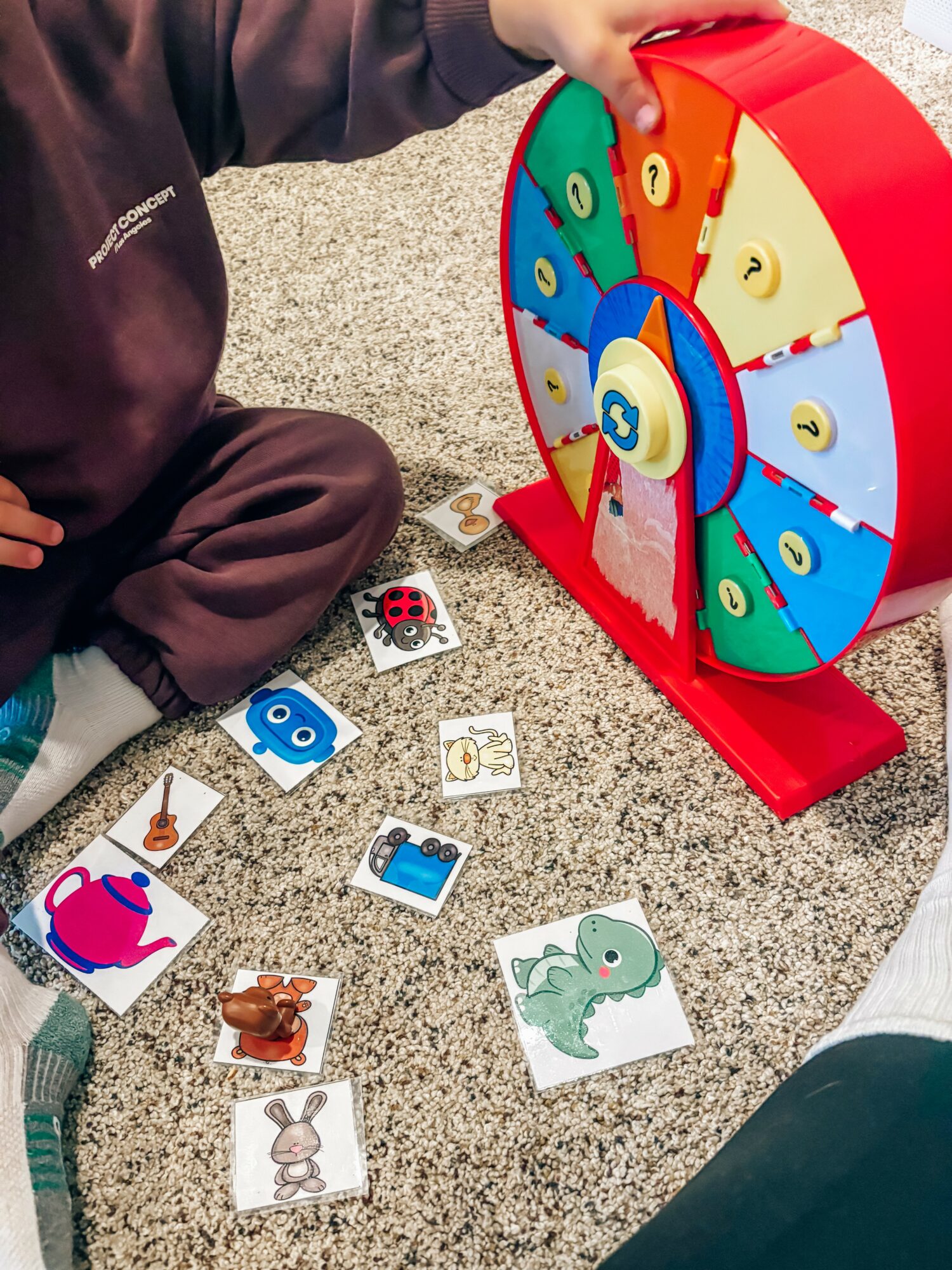 Children's hands and legs around a colorful spinning wheel and animal picture cards on the floor.