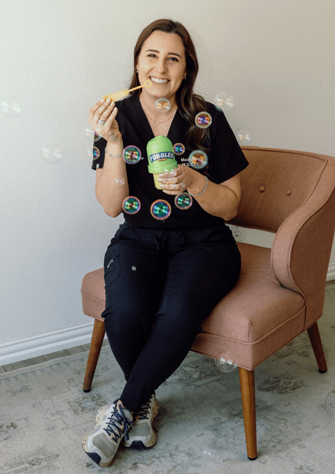 Woman sitting on a pink chair, eating ice cream, surrounded by floating colorful stickers, smiling, in a room with a white wall.