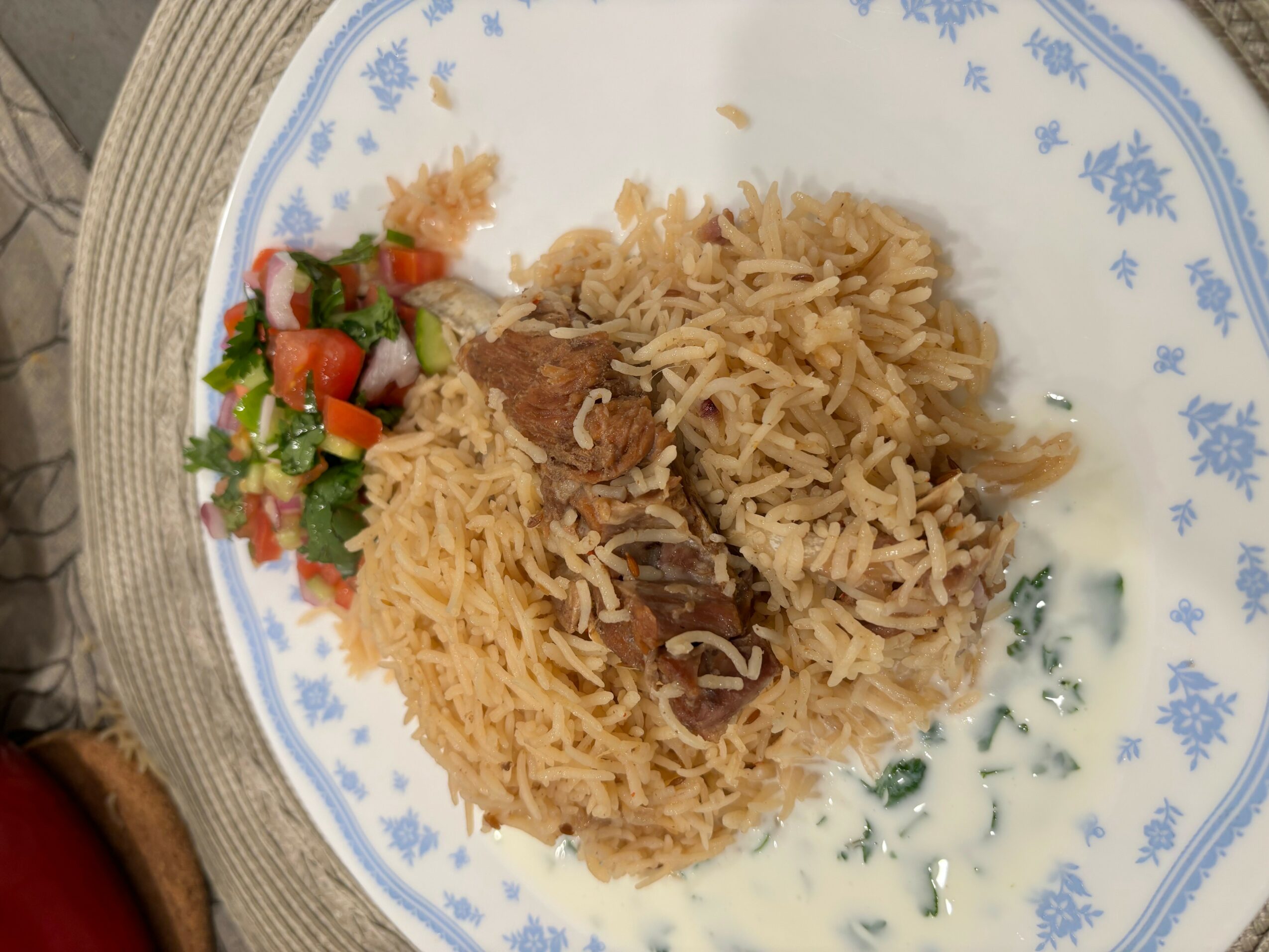 Plate with rice, meat, and salad, viewed from above, on a patterned tablecloth.