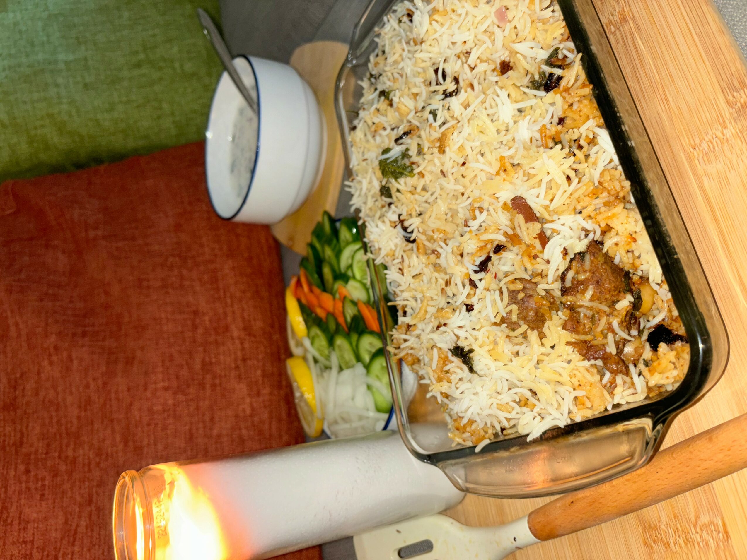 Baked casserole dish topped with cheese, side of sliced vegetables, and a bowl of sauce on a wooden table.