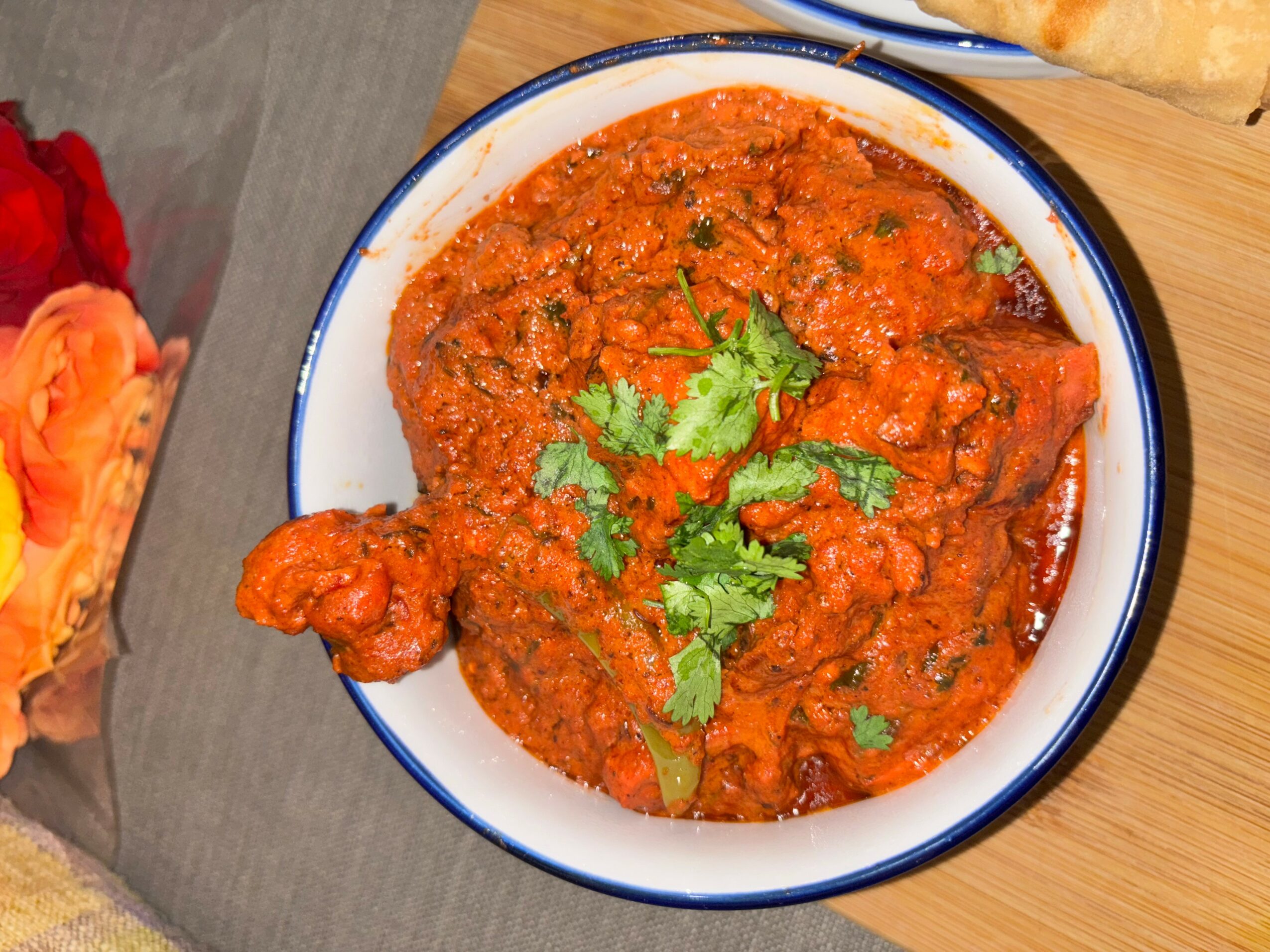 Bowl of spicy tomato-based curry garnished with cilantro, served on a wooden surface.