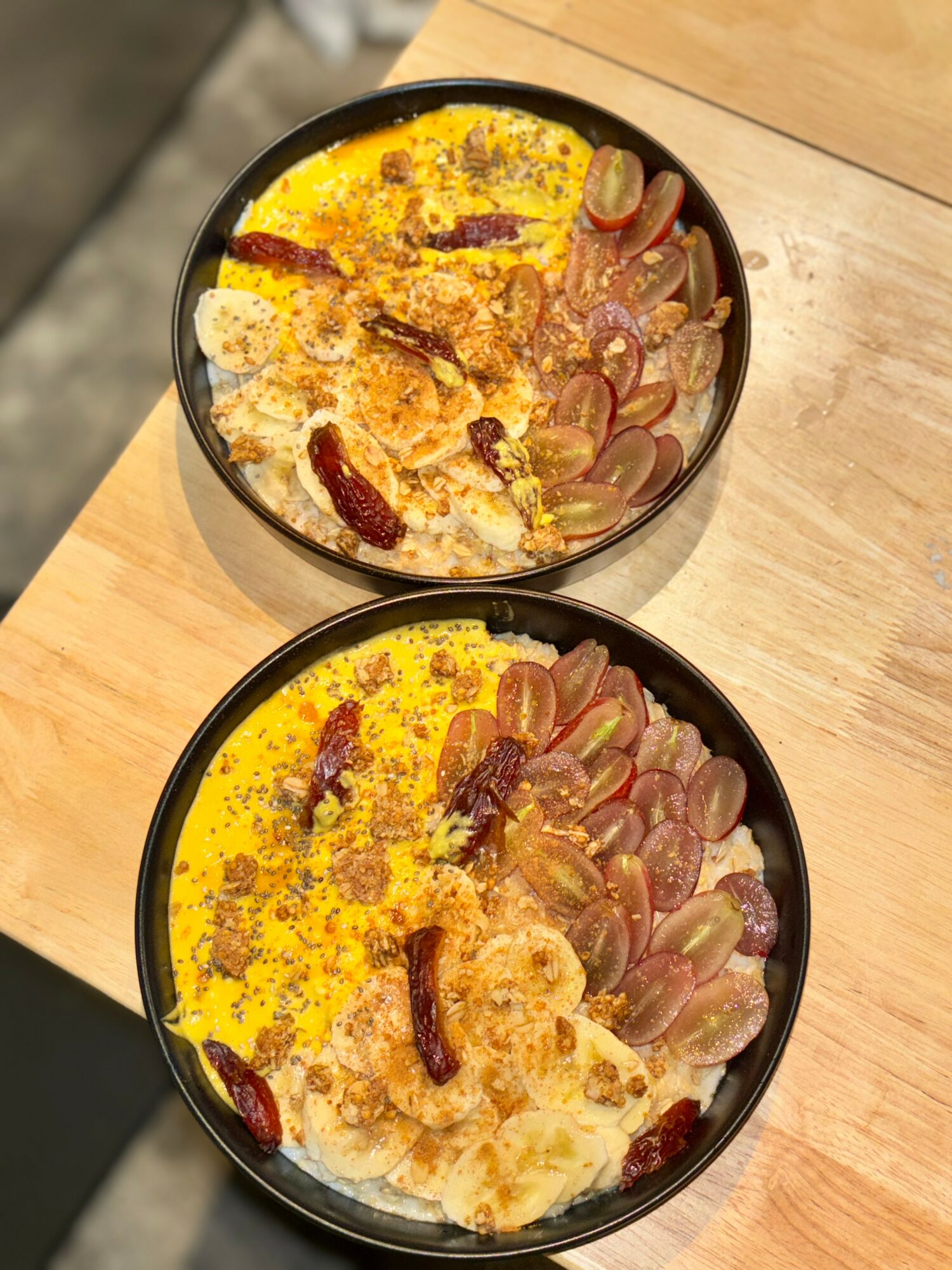 Two bowls of rice topped with sliced grapes, dried chili peppers, and yellow seasoning on a wooden table.