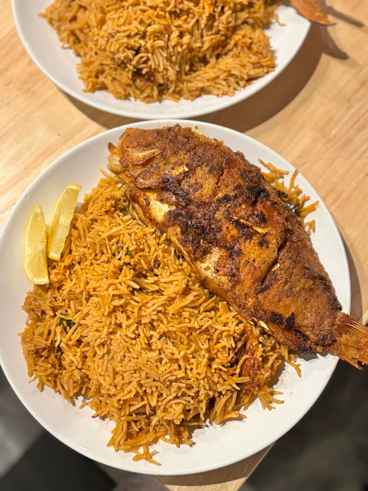 Plate with fried fish, rice, and lemon wedge on a wooden table.