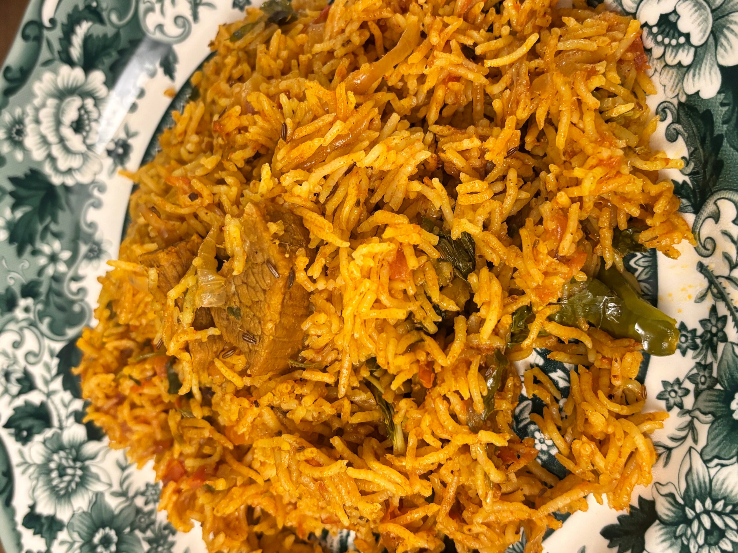 Plate of yellow rice with vegetables and meat, garnished with green beans, on a decorative plate.