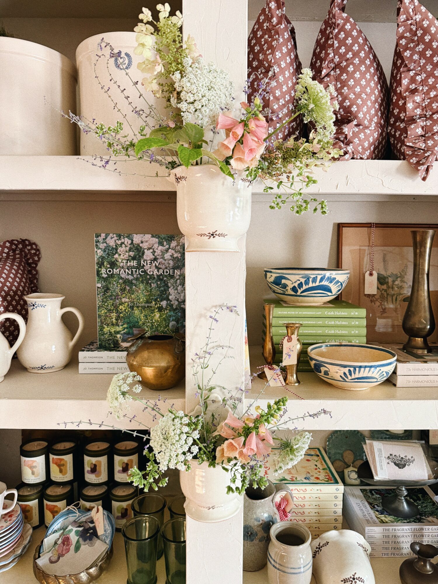 Shelves with vases, books, teapots, and decorative items, including flowers in a white vase, arranged on white shelves.
