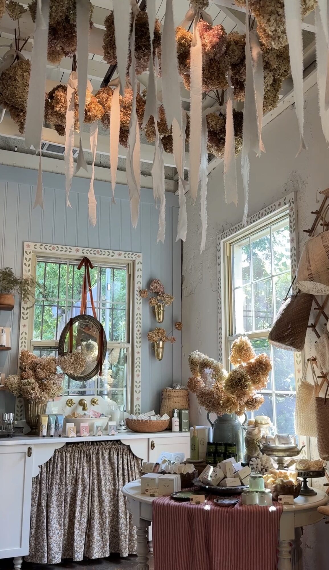 Room decorated with hanging paper flowers, a window with natural light, and a table with various items, including flowers and a lamp.