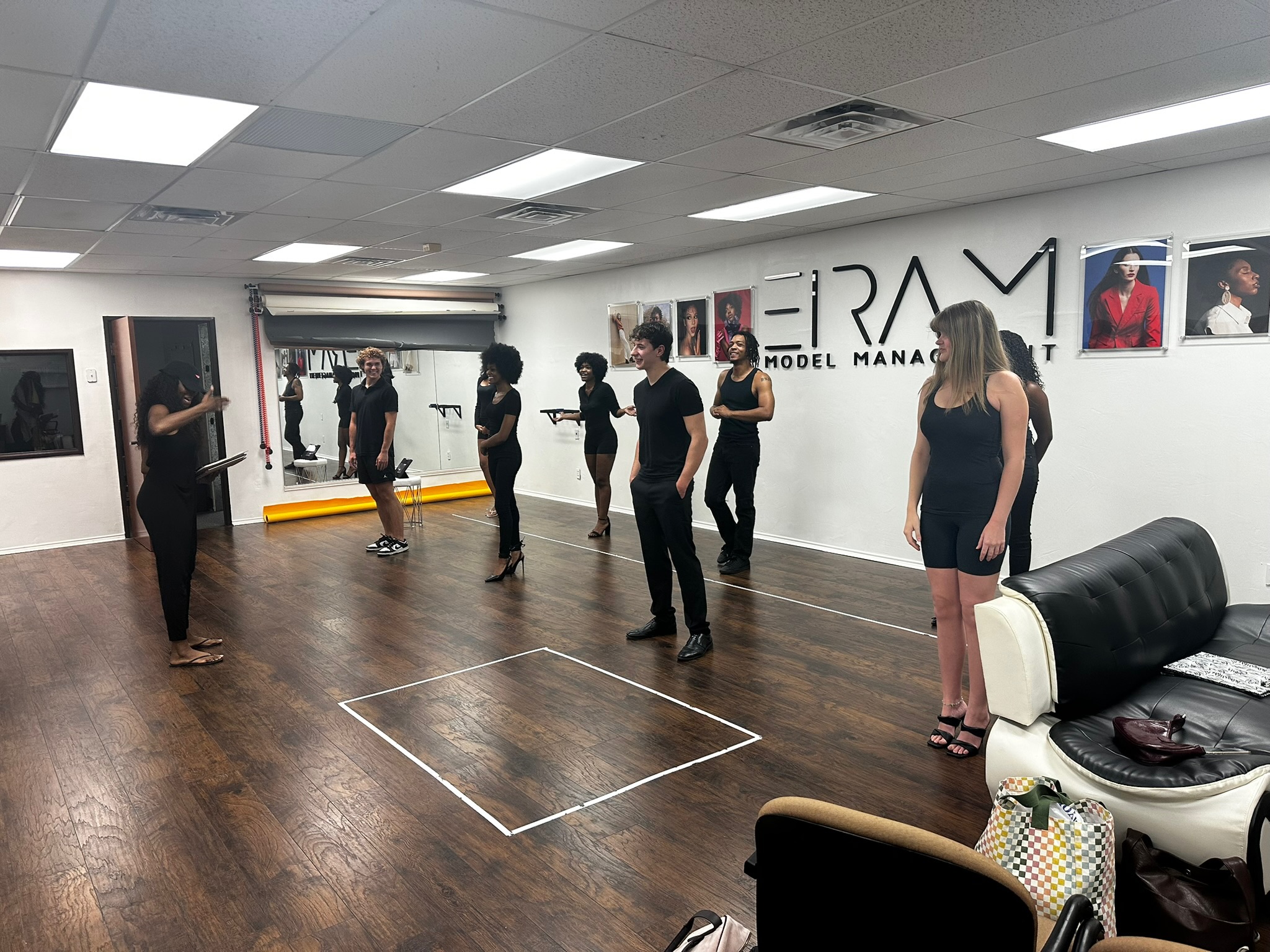 People standing in a dance studio with mirrors, wooden floor, and framed photos on the wall, practicing dance moves.