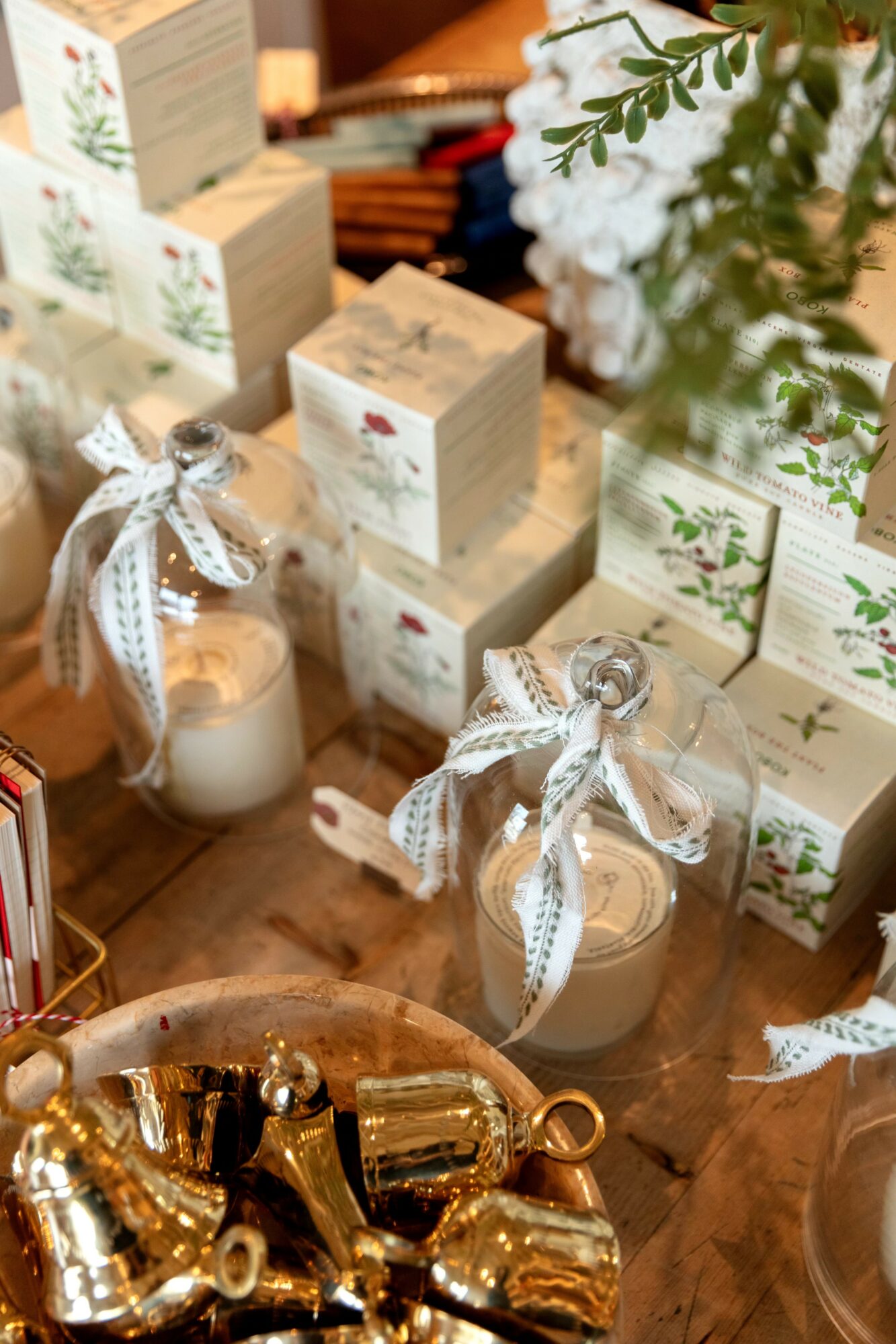 Decorative candles with ribbons, gift boxes, and greenery on a wooden surface, festive holiday setting.