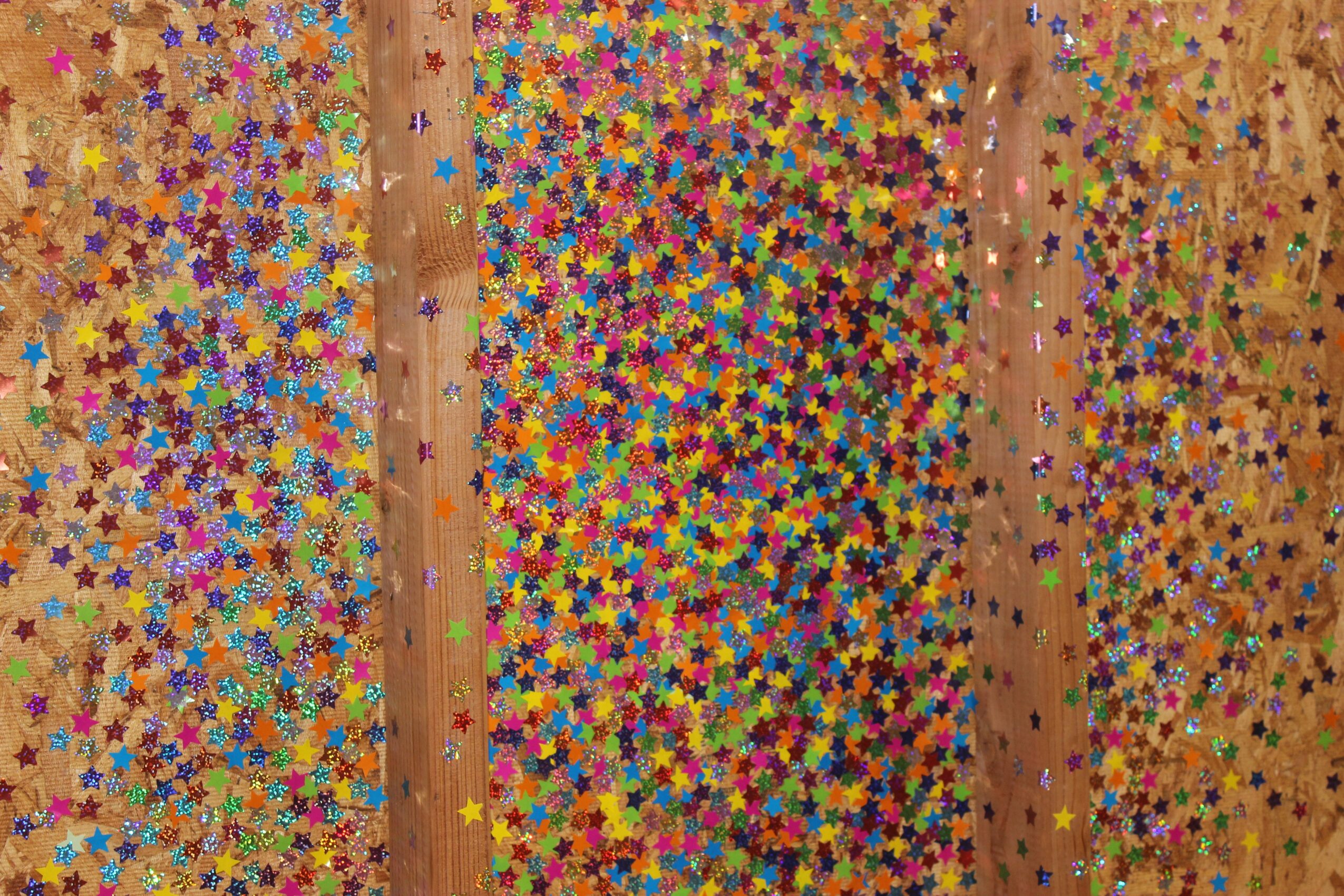 Colorful star-shaped confetti scattered on a wooden surface with three vertical wooden strips.
