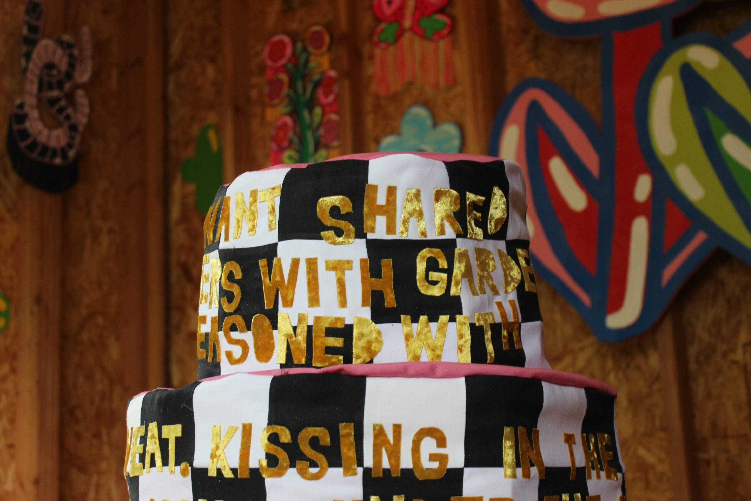 Part of a decorated cake with black, white, and gold lettering, and colorful background elements.