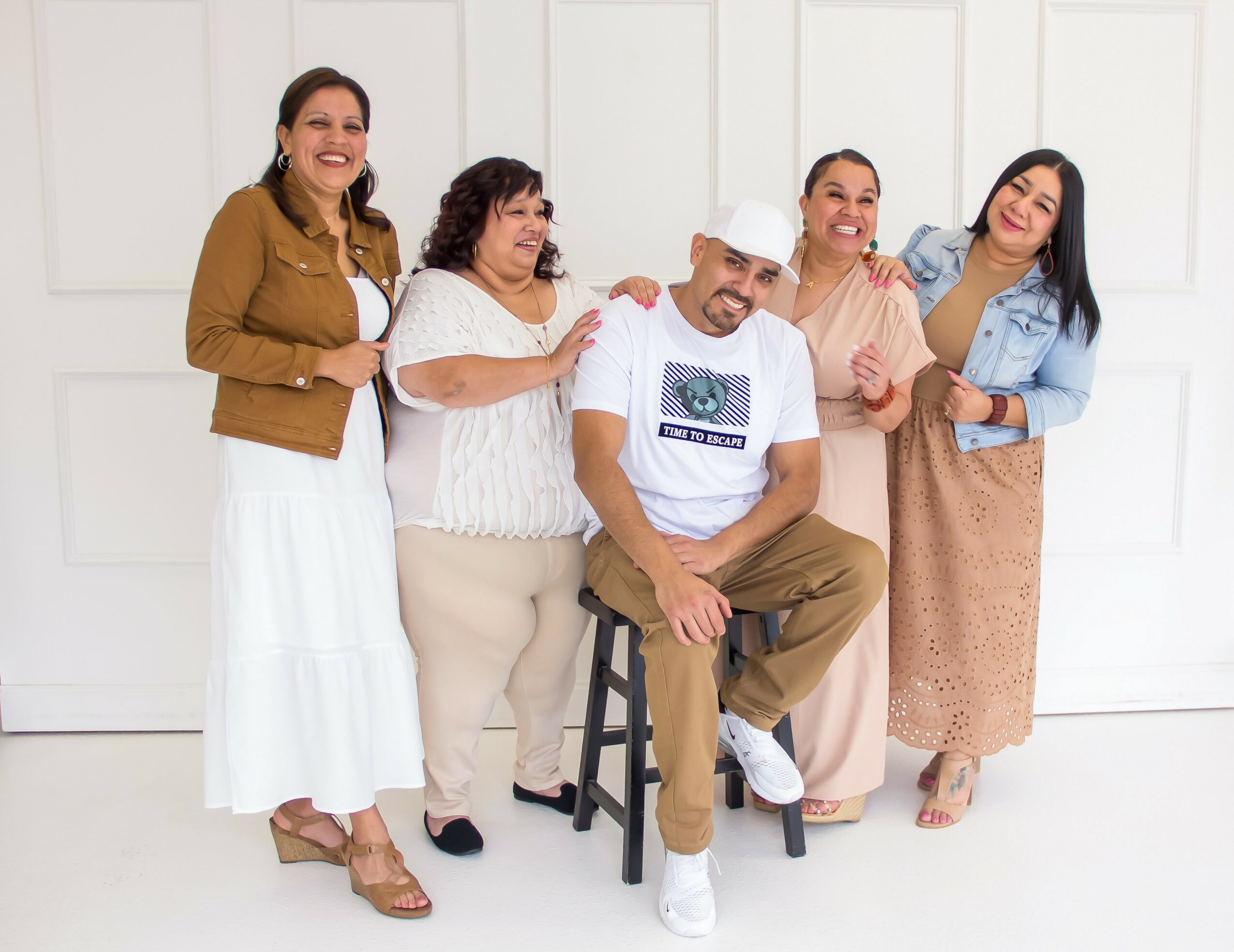 Group of five people smiling, standing and sitting against a white background, with one person in a chef's hat. Word count: 20