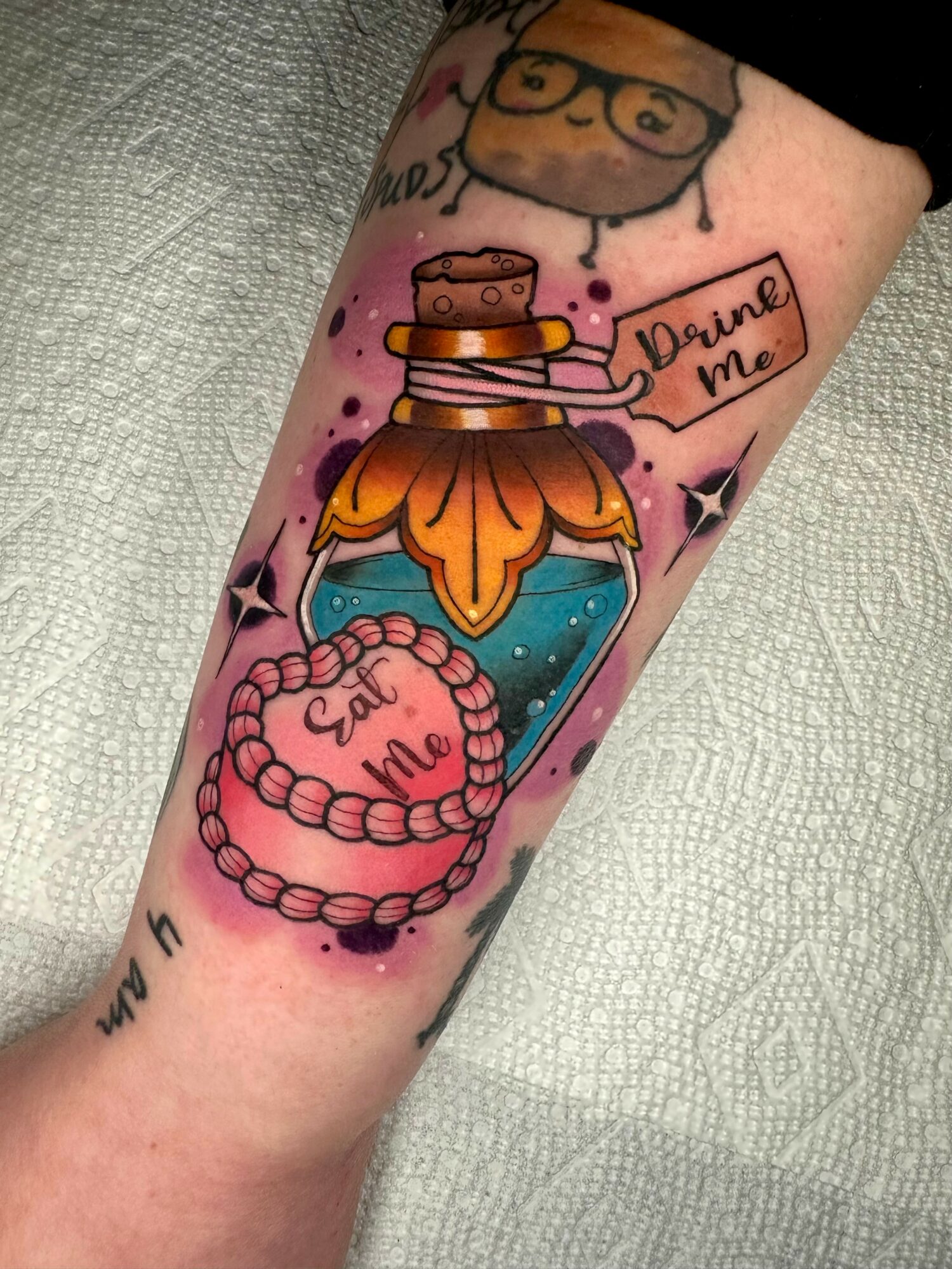 Tattoo of a perfume bottle with a heart-shaped beaded necklace, a cartoon face, and a speech bubble saying 'Dare me'.