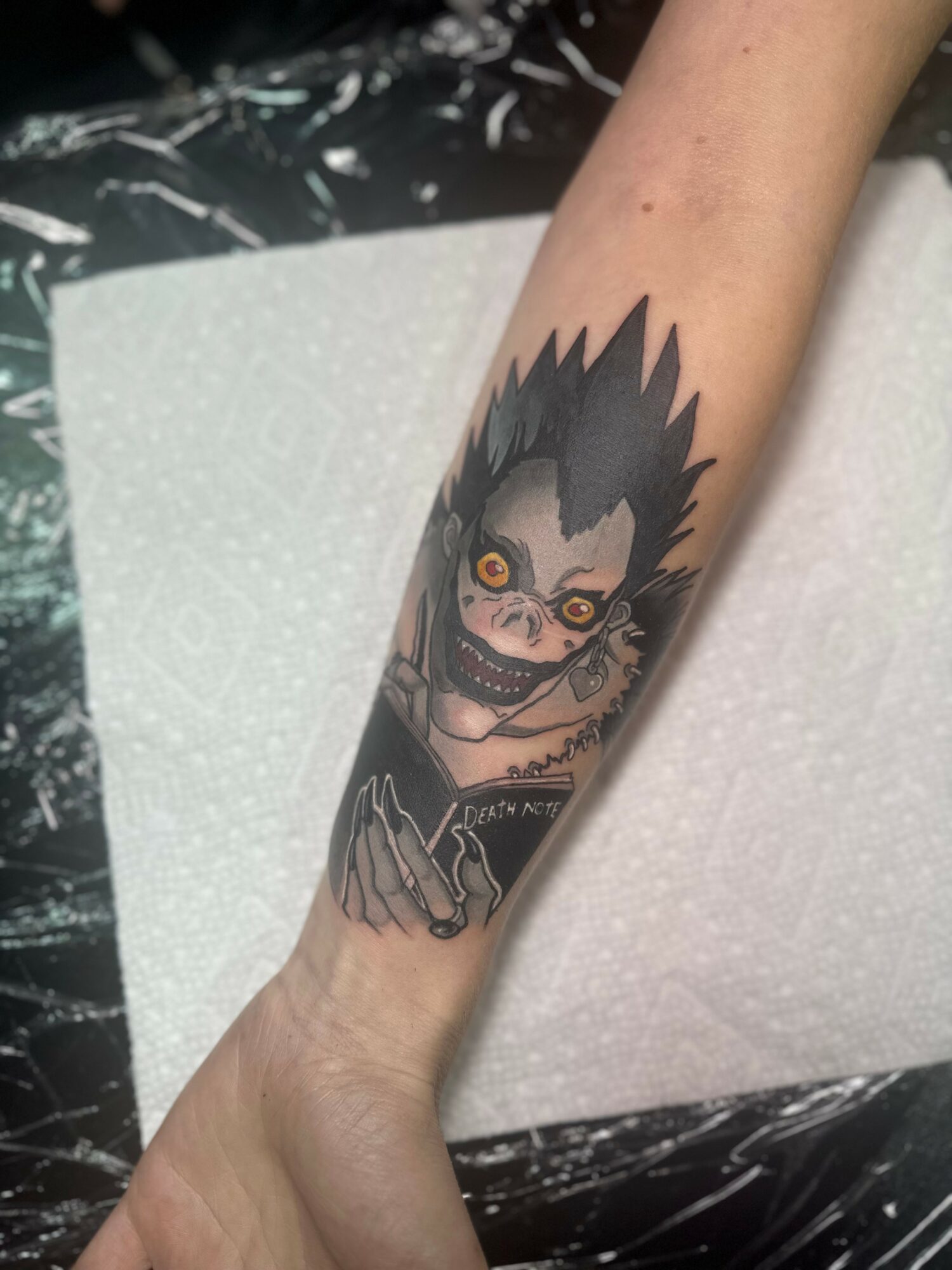 Tattoo of a character with spiky hair, glasses, and a wide grin on the forearm.