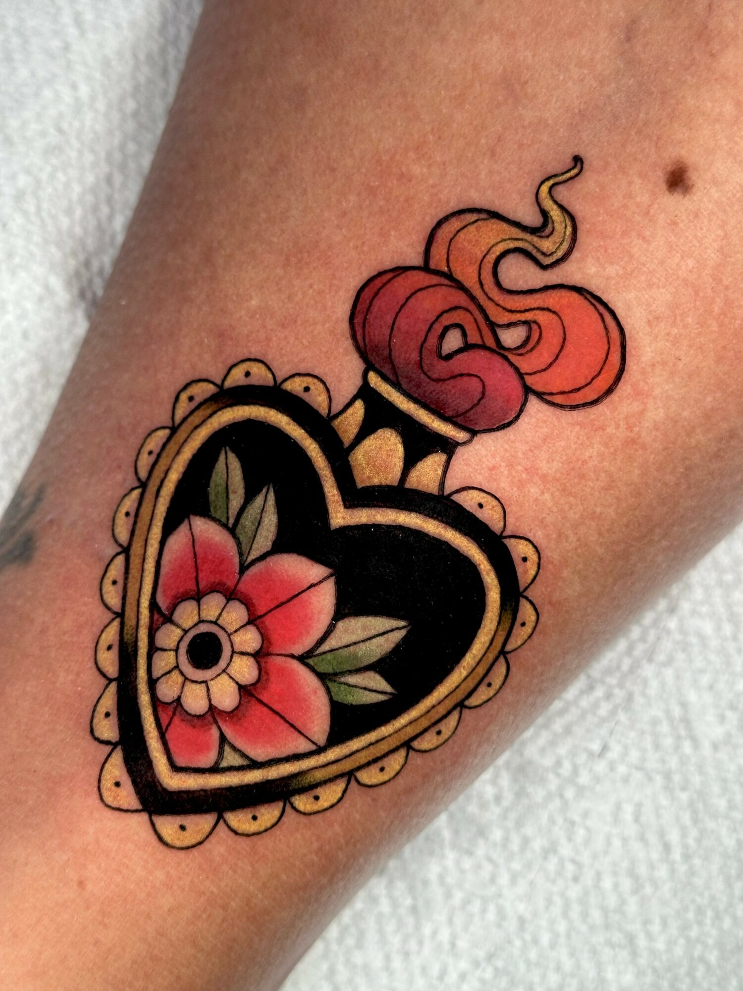 Tattoo of a heart-shaped locket with a flower inside and a woman with flowing hair above it.