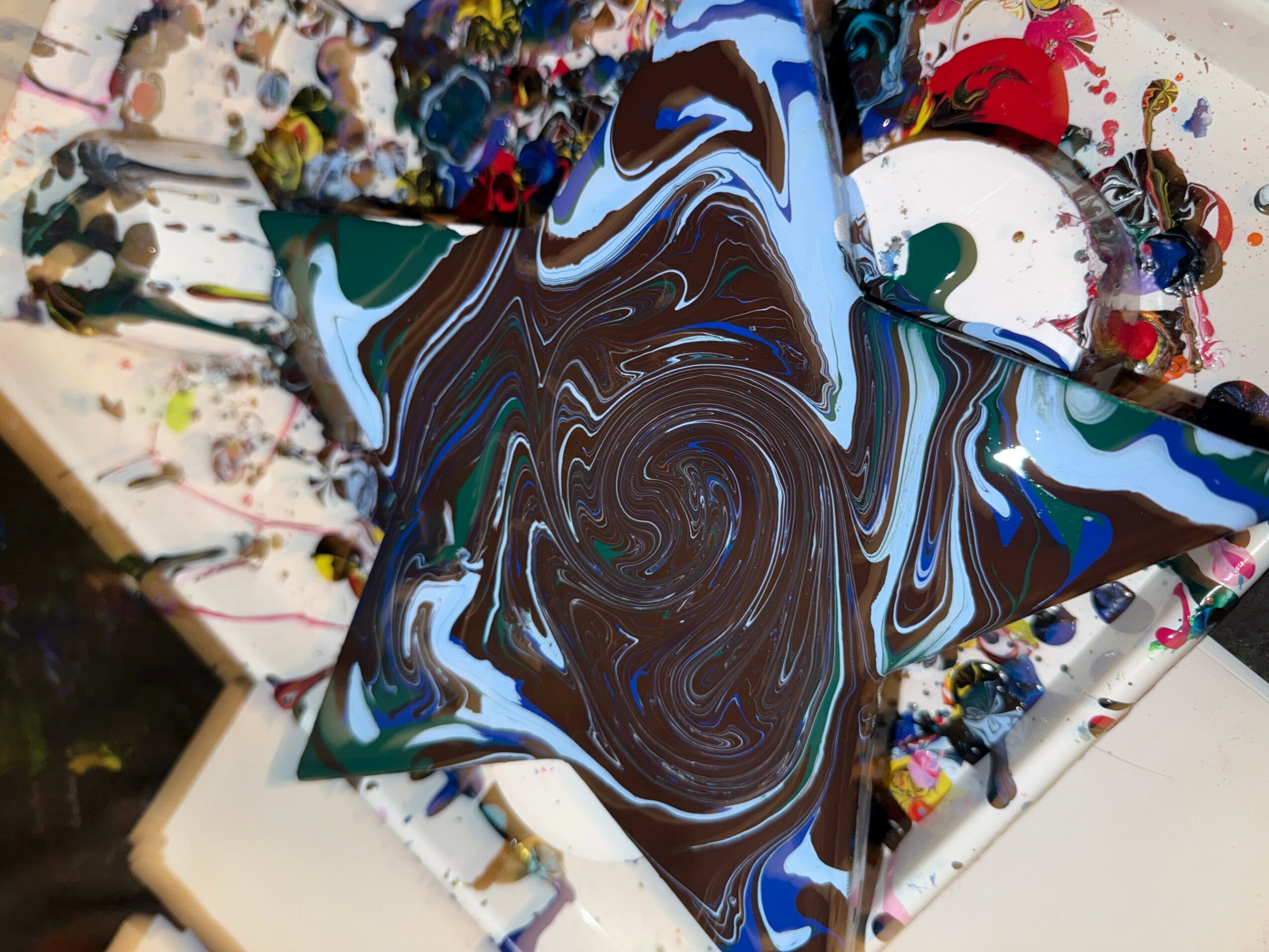 Swirling abstract pattern with brown, blue, and white colors on a star-shaped object, surrounded by paint splatters.