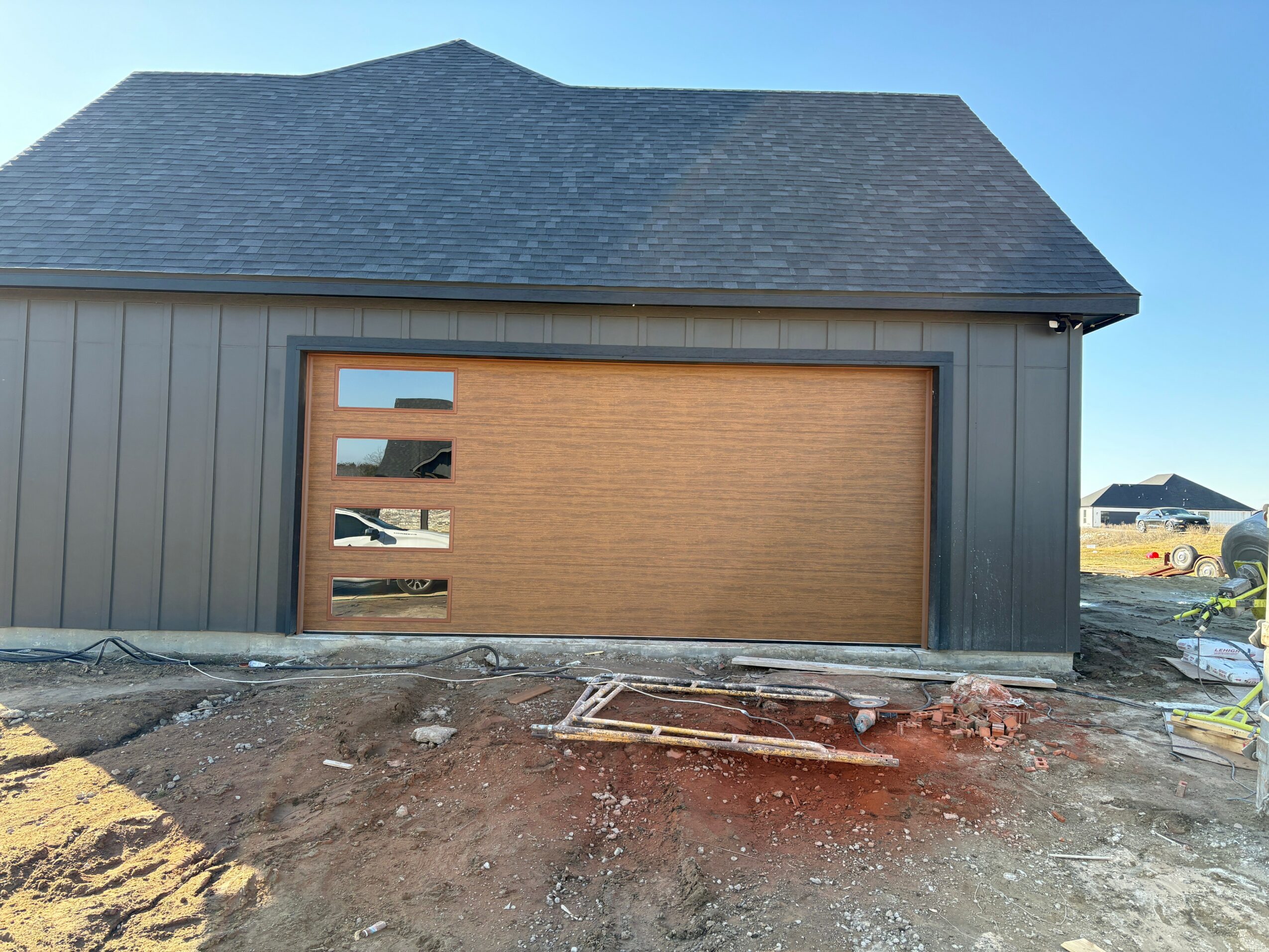 Building with a garage door, construction site with dirt and debris in front, clear blue sky, and neighboring structures in background.