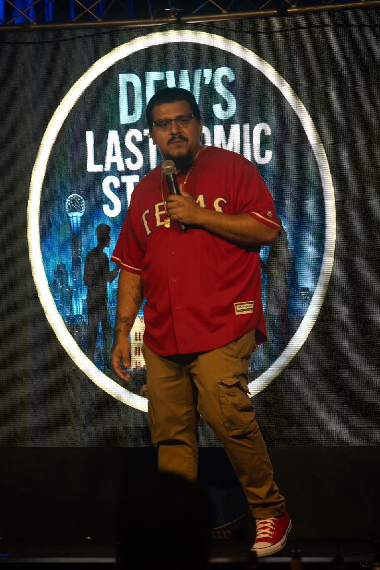 Man holding microphone on stage with a circular backdrop displaying text and cityscape silhouette.