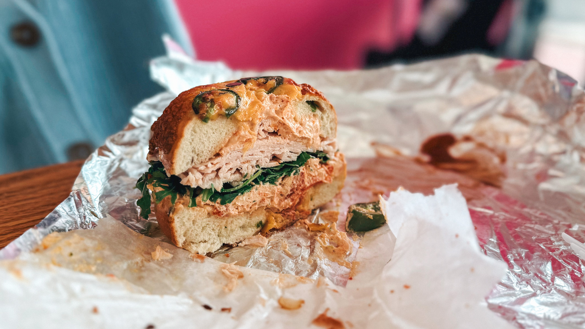 Half-eaten sandwich with lettuce and meat on crumpled foil, with some sauce and crumbs, on a wooden surface.